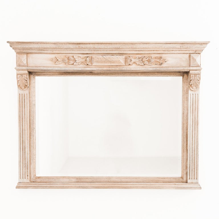 A bleached oak mirror from Belgium produced circa 1900. Fluted side supports crowned by an acanthus stretch upwards to support a decorated lintel underneath a cornice. These architectural elements display this piece’s neoclassical pedigree. Composed