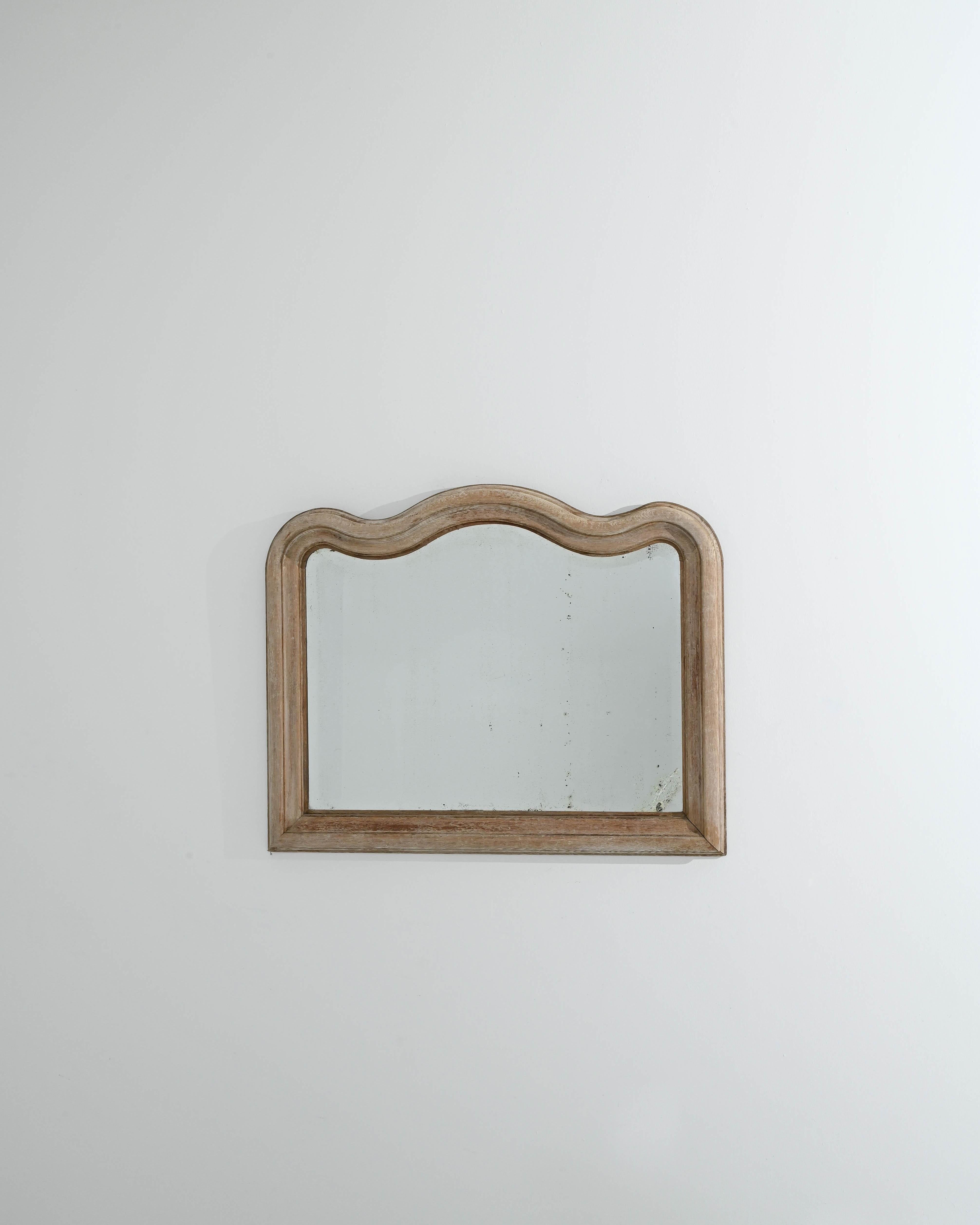 Made circa 1900 in Belgium, this antique mirror showcases a masterfully crafted oak frame. The looking glass is adorned with smooth, wavy outlines that grace its crown, creating a captivating contrast with the sharp angularity of the lower frame.