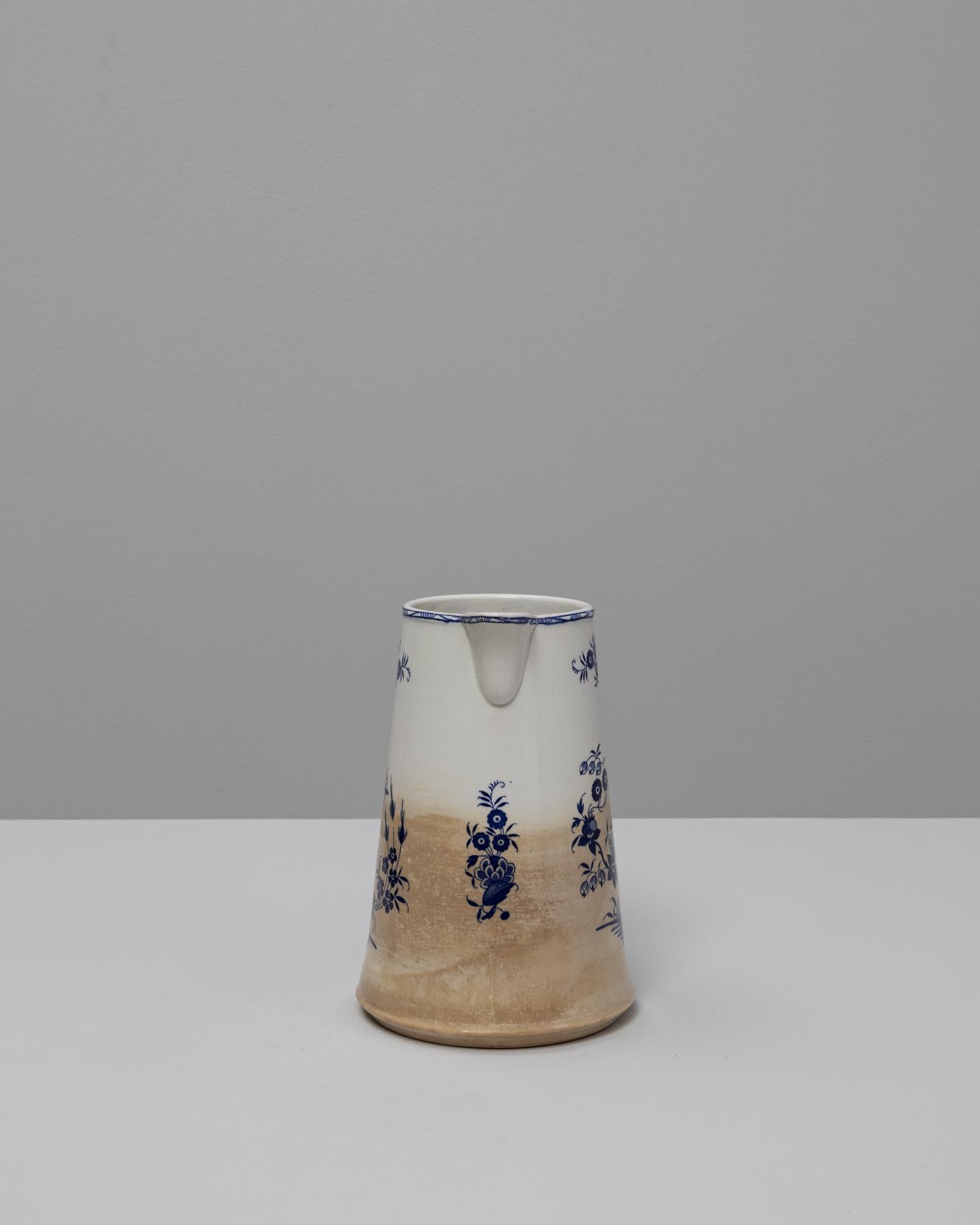 Questa brocca in ceramica belga blu Chinoiserie del 1900 fonde l'artigianato europeo con motivi decorativi di ispirazione orientale, creando un pezzo affascinante e senza tempo. La sua forma affusolata e il manico angolare evocano le prime ceramiche