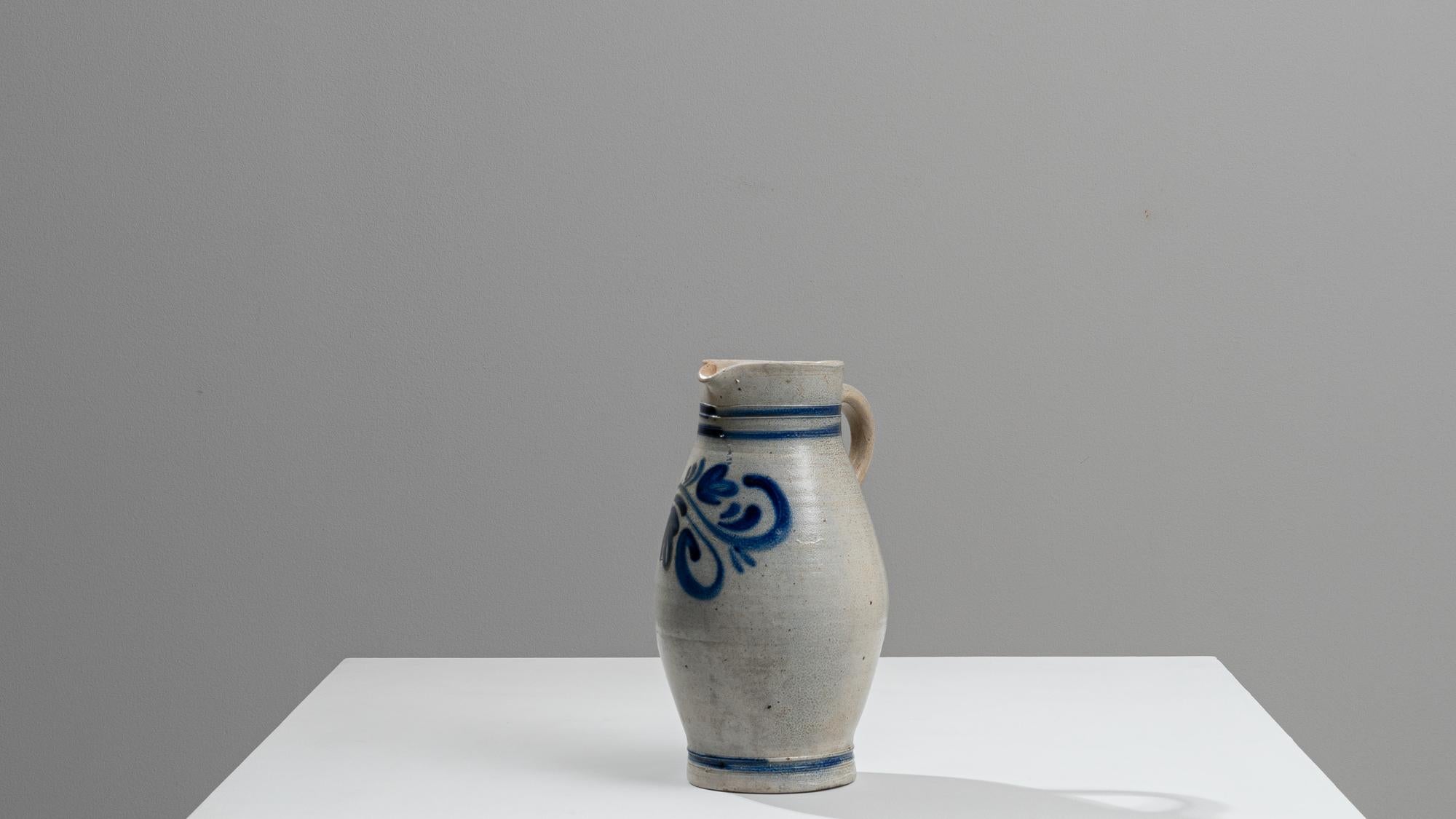 This 1900s Belgian ceramic jug showcases the understated beauty and elegance of early 20th-century European pottery. The jug's sturdy form is beautifully crafted from a speckled grey ceramic, enhanced with bold blue stripes and a simplistic eye