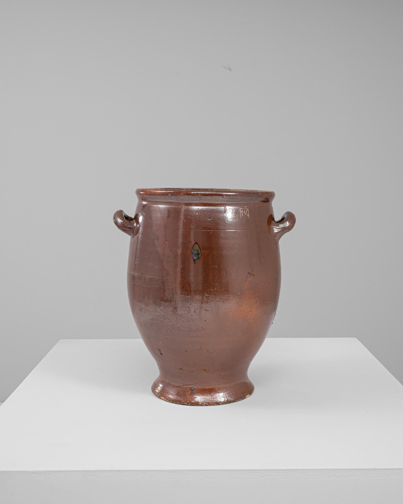 Questo vaso in ceramica belga del 1900 presenta una classica forma arrotondata con manici graziosamente curvati e una calda finitura marrone smaltata. La sua superficie liscia e le sottili variazioni di tono evidenziano la lavorazione artigianale