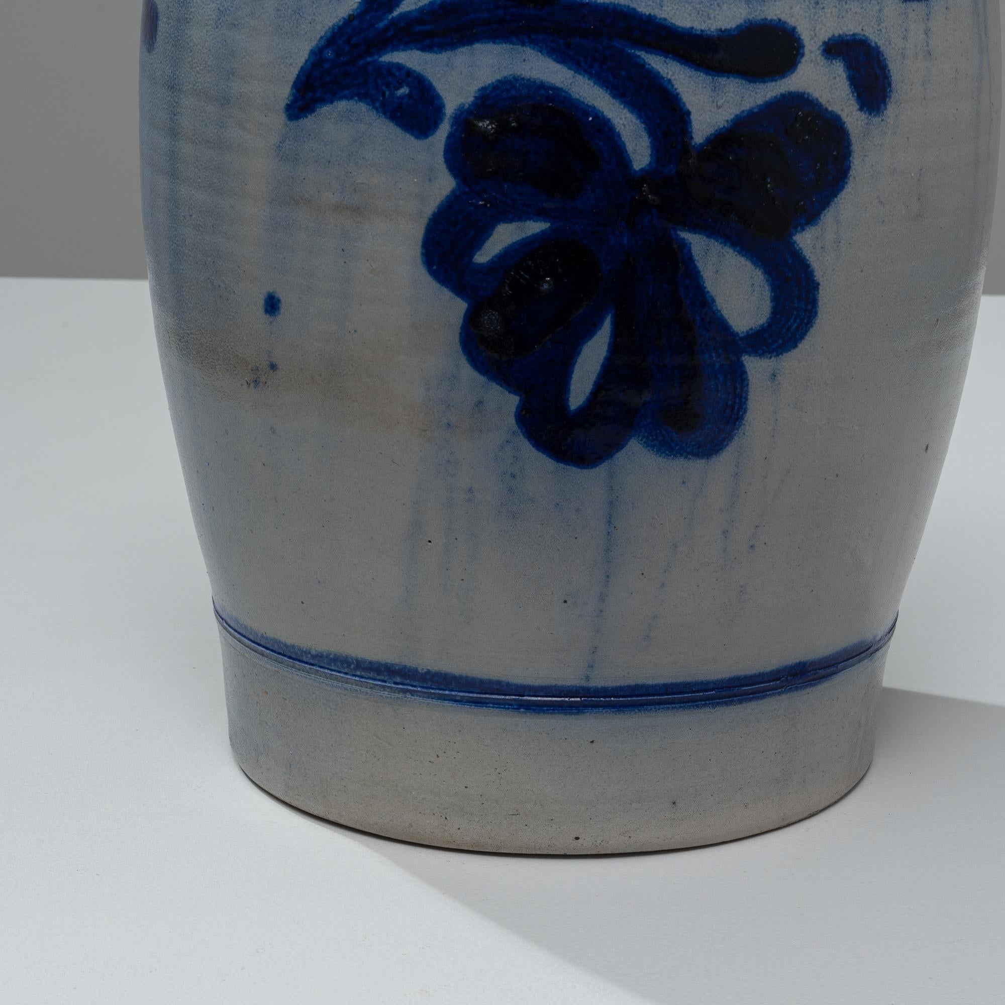 Ce pot en céramique belge du début des années 1900 est un chef-d'œuvre d'élégance rustique et de charme vintage, idéal pour ceux qui apprécient la beauté de l'artisanat. Le pot présente un corps robuste et arrondi, orné de motifs floraux bleus