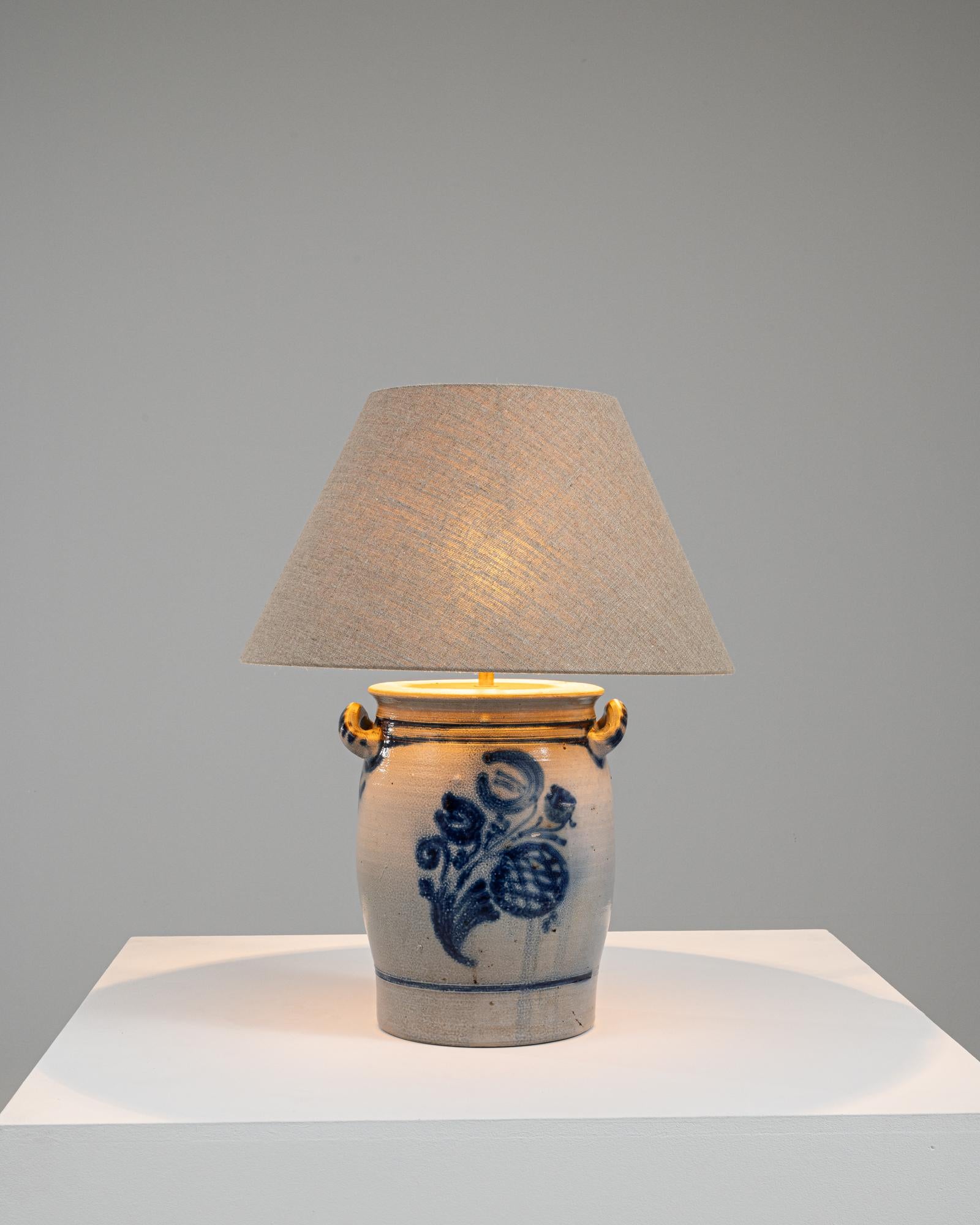 Immerse yourself in the captivating charm of this 1900s Belgian ceramic table lamp, a piece that beautifully merges artistic heritage with functionality. The base of the lamp is a classic Belgian ceramic pot, adorned with a striking blue floral