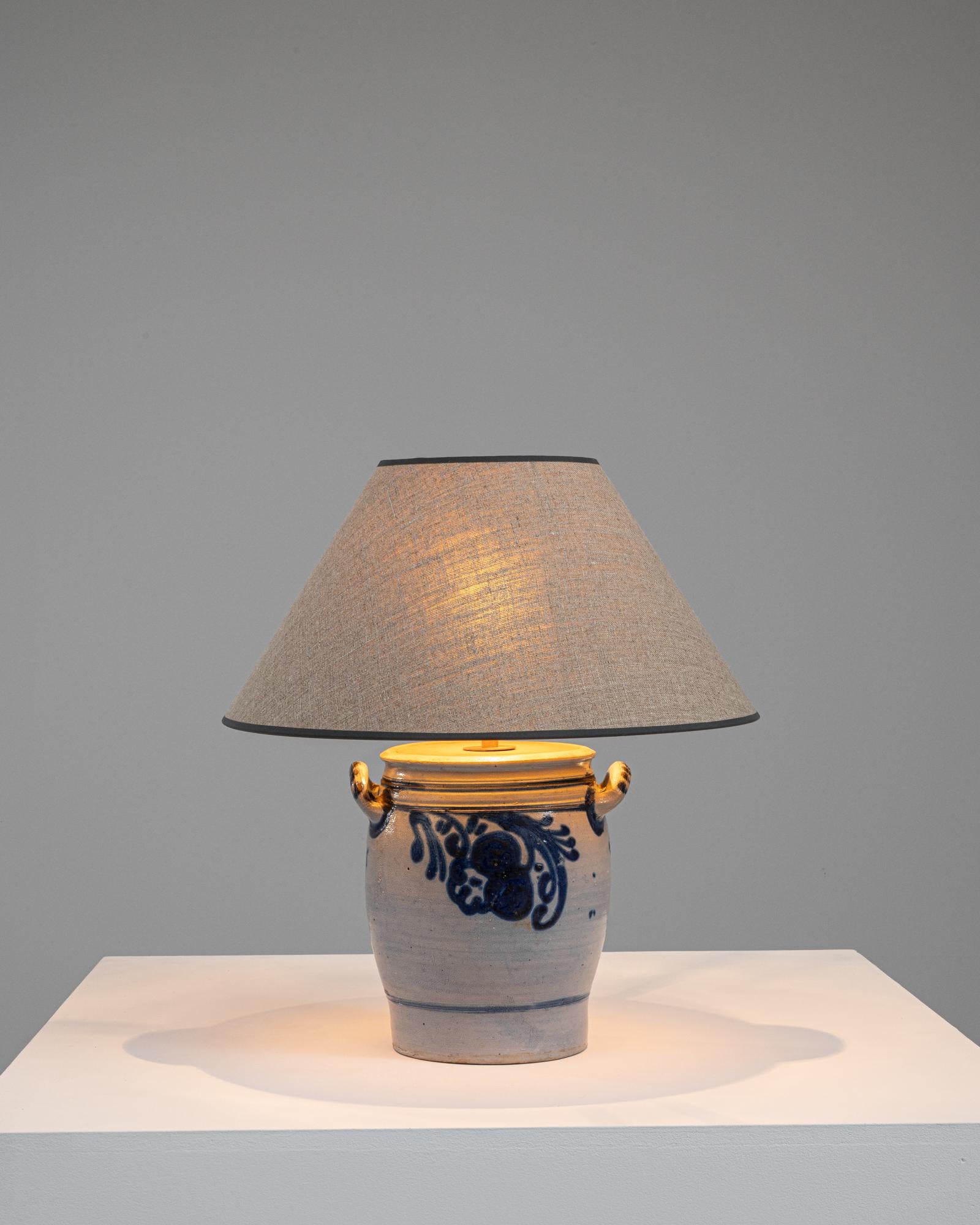 Cette lampe de table en céramique belge des années 1900 est une délicieuse fusion d'artisanat historique et de charme pittoresque. La base en céramique robuste, ornée d'un motif floral bleu distinctif sur un fond gris doux, capture l'essence de la