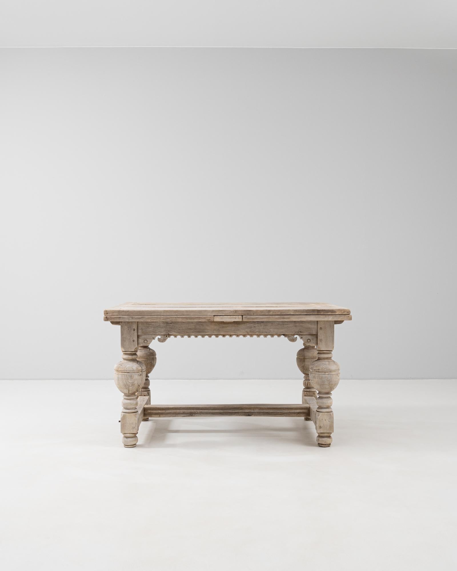 This 1900s Belgian folding table is a beautifully crafted piece that balances functionality with sculptural detail. Constructed from solid wood with a bleached finish that highlights its natural grain, the table features substantial turned legs, a