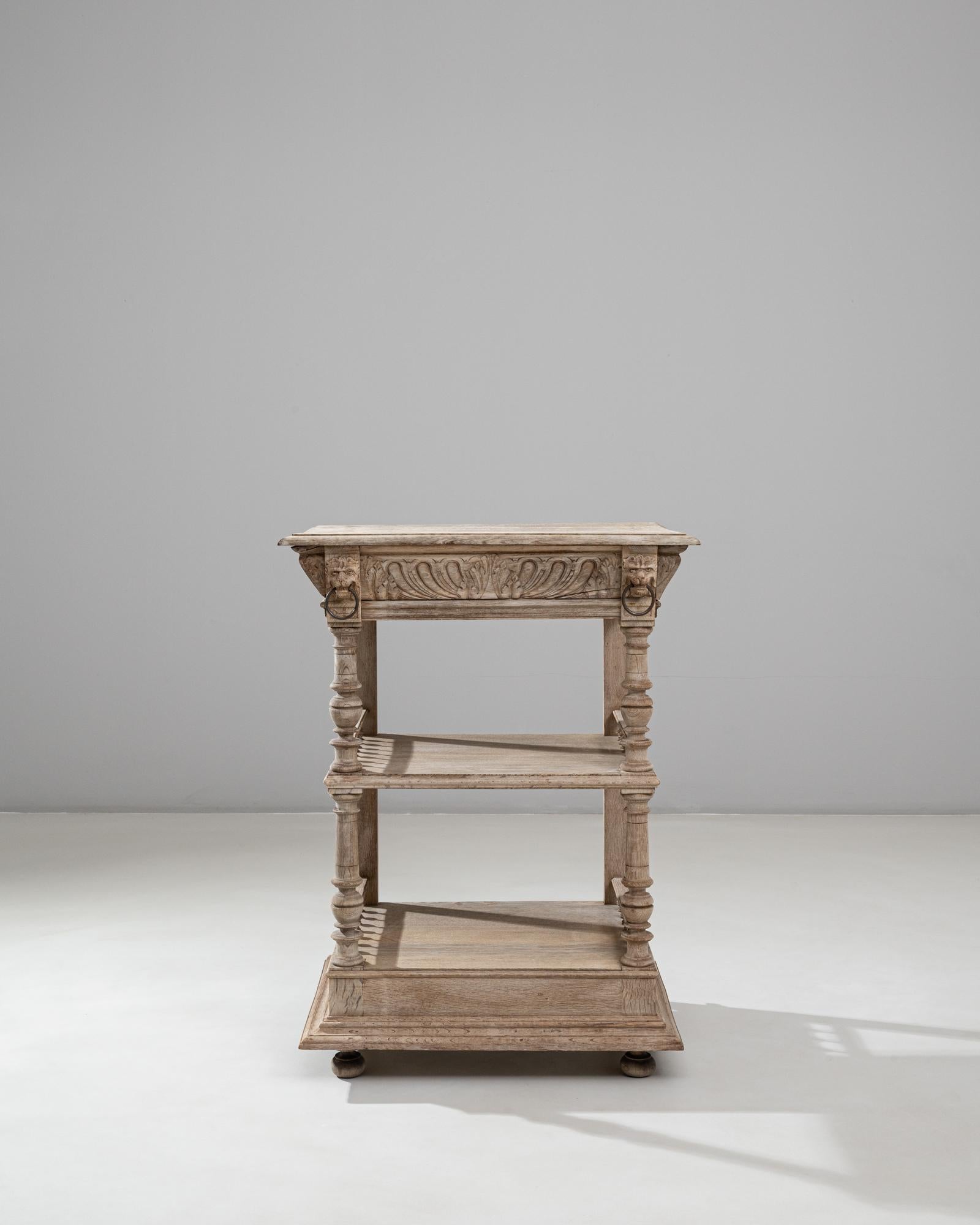 This 1900s Belgian hand-carved oak bedside table showcases exceptional craftsmanship and decorative detail across its elegant tiered form. The top is framed by intricately carved acanthus motifs, complemented by small ring pulls on each side that