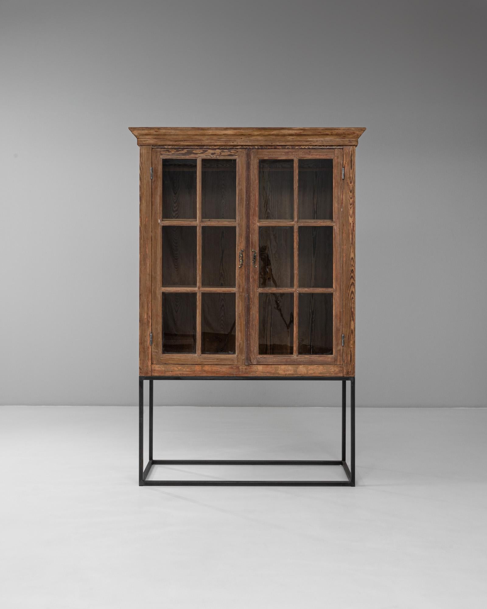 Questa vetrina belga in legno del 1900 unisce un design utilitario a un carattere senza tempo. Realizzato con una semplice forma rettangolare e con ante in vetro, mostra le venature naturali del legno esaltate da una calda patina dovuta all'età e