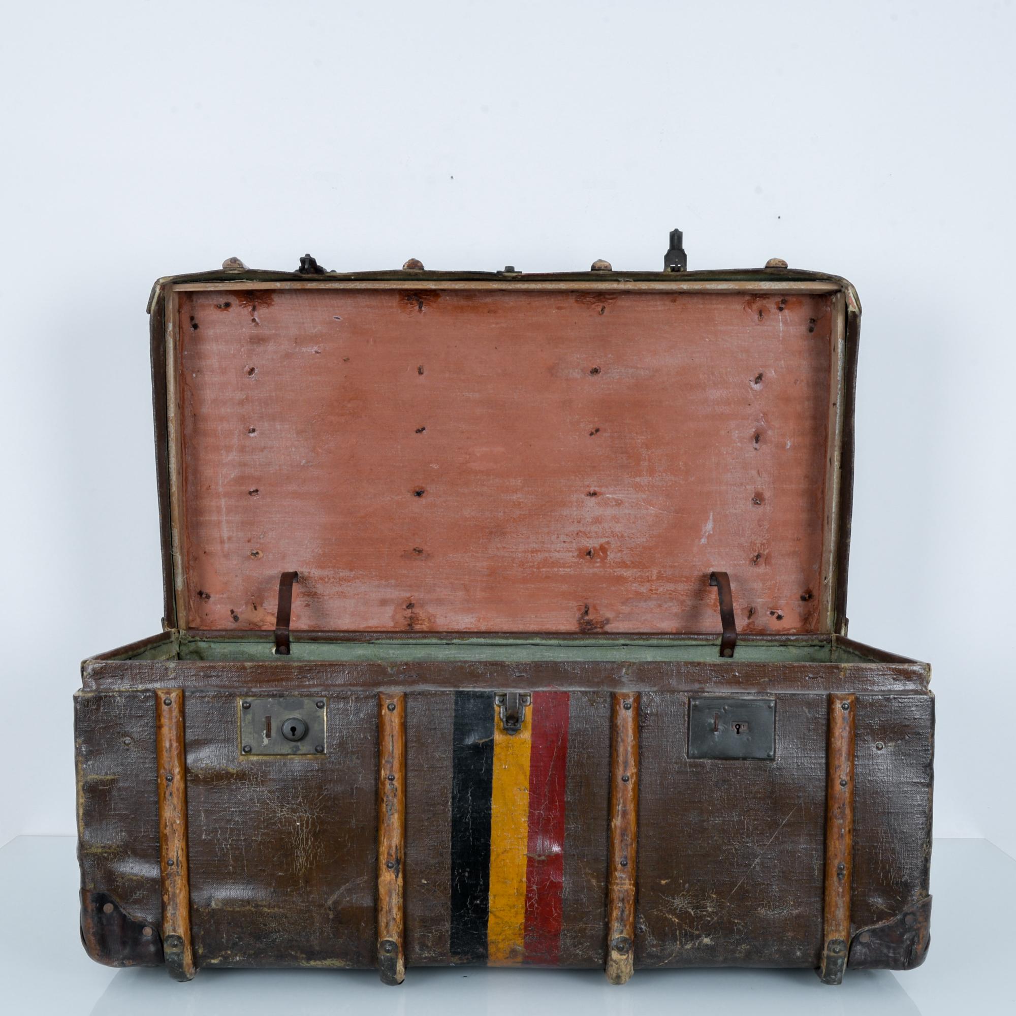 This leather suitcase was made in Belgian, circa 1900. The top lid can be fastened to the three front clasps. Curved wooden rods, reinforced by metal protect the trunk from damage. The colors of the Belgian flag are painted in the center of this