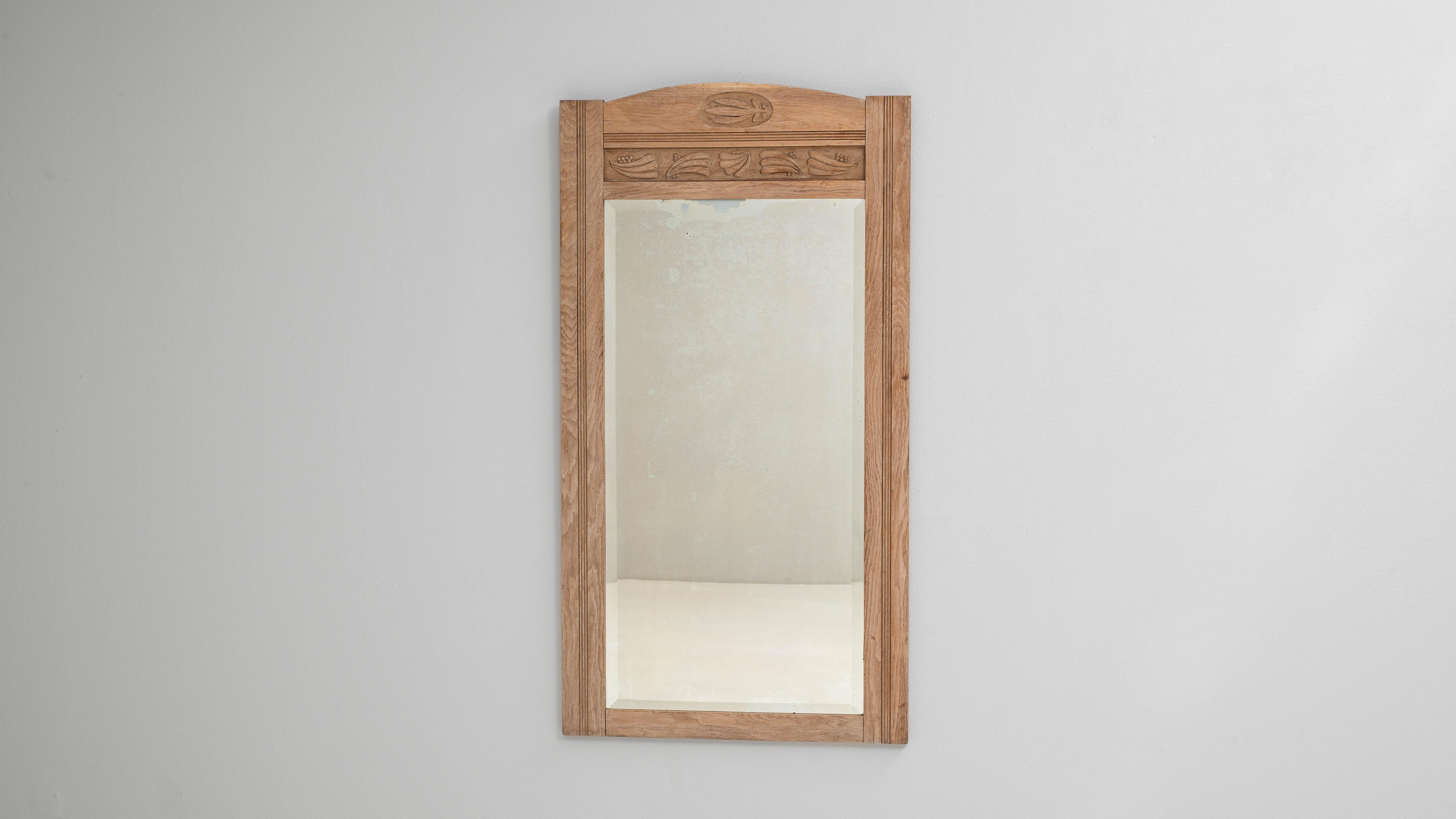 Uno specchio in quercia belga del 1900 con dettagli intagliati che evidenziano la sobria maestria dell'artigianato belga dei primi del Novecento. La cornice è composta da rovere delicatamente patinato, il cui tono caldo enfatizza le linee verticali