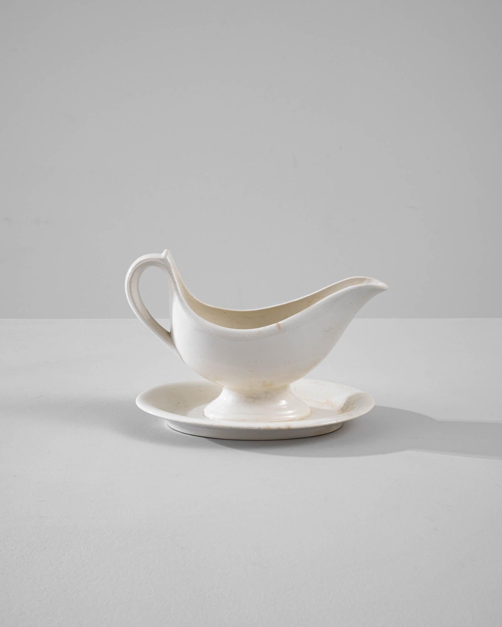 A vintage porcelain sauce boat made in Belgium, circa 1900. White china is finished with a luscious glossy glaze, elevating the superior form and subtle vintage patina of this finely crafted table piece. The delicate contour and out-turned lip of