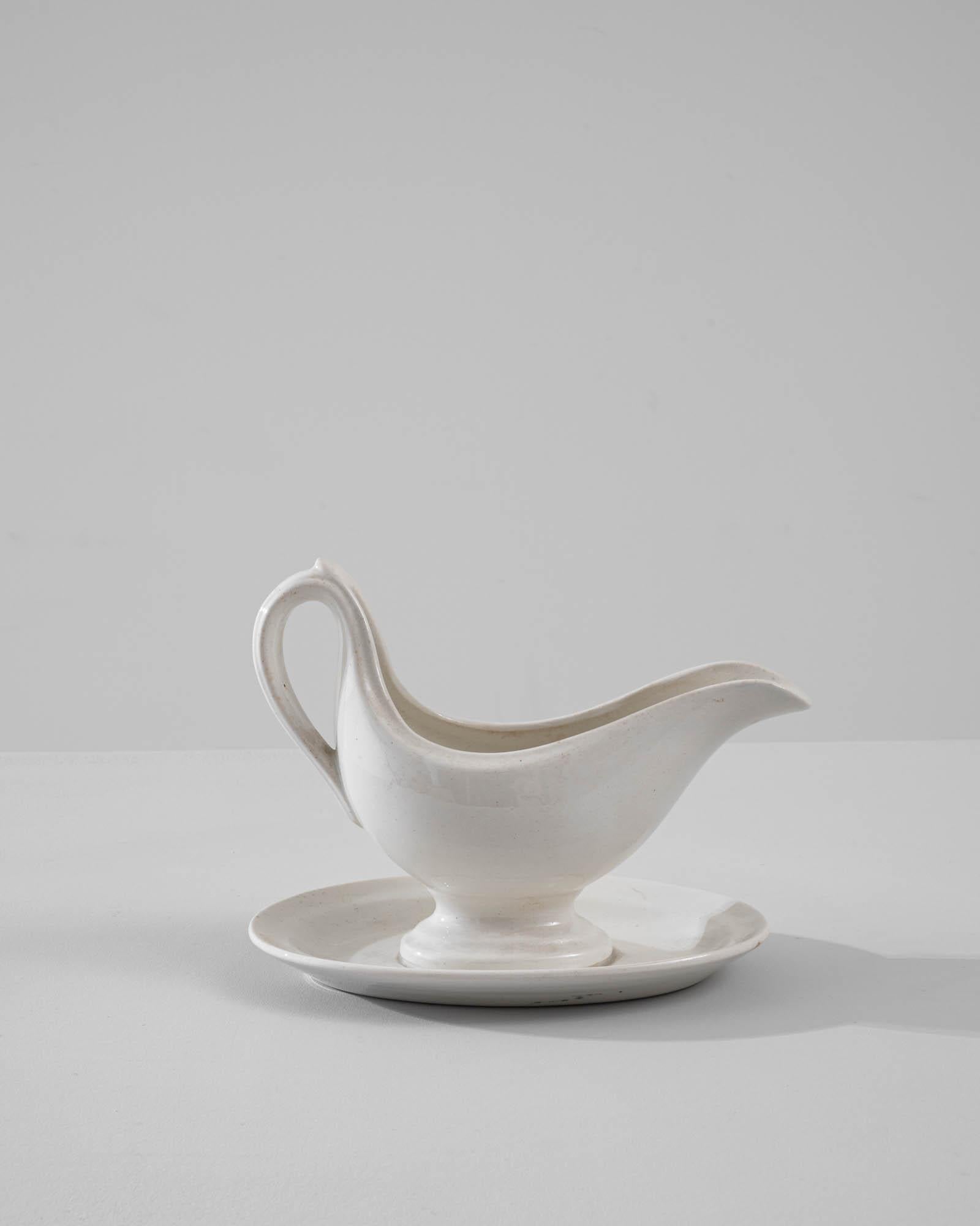 A vintage porcelain sauce boat made in Belgium, circa 1900. White china is finished with a luscious glossy glaze, elevating the superior form and subtle vintage patina of this finely crafted table piece. The delicate contour and out-turned lip of