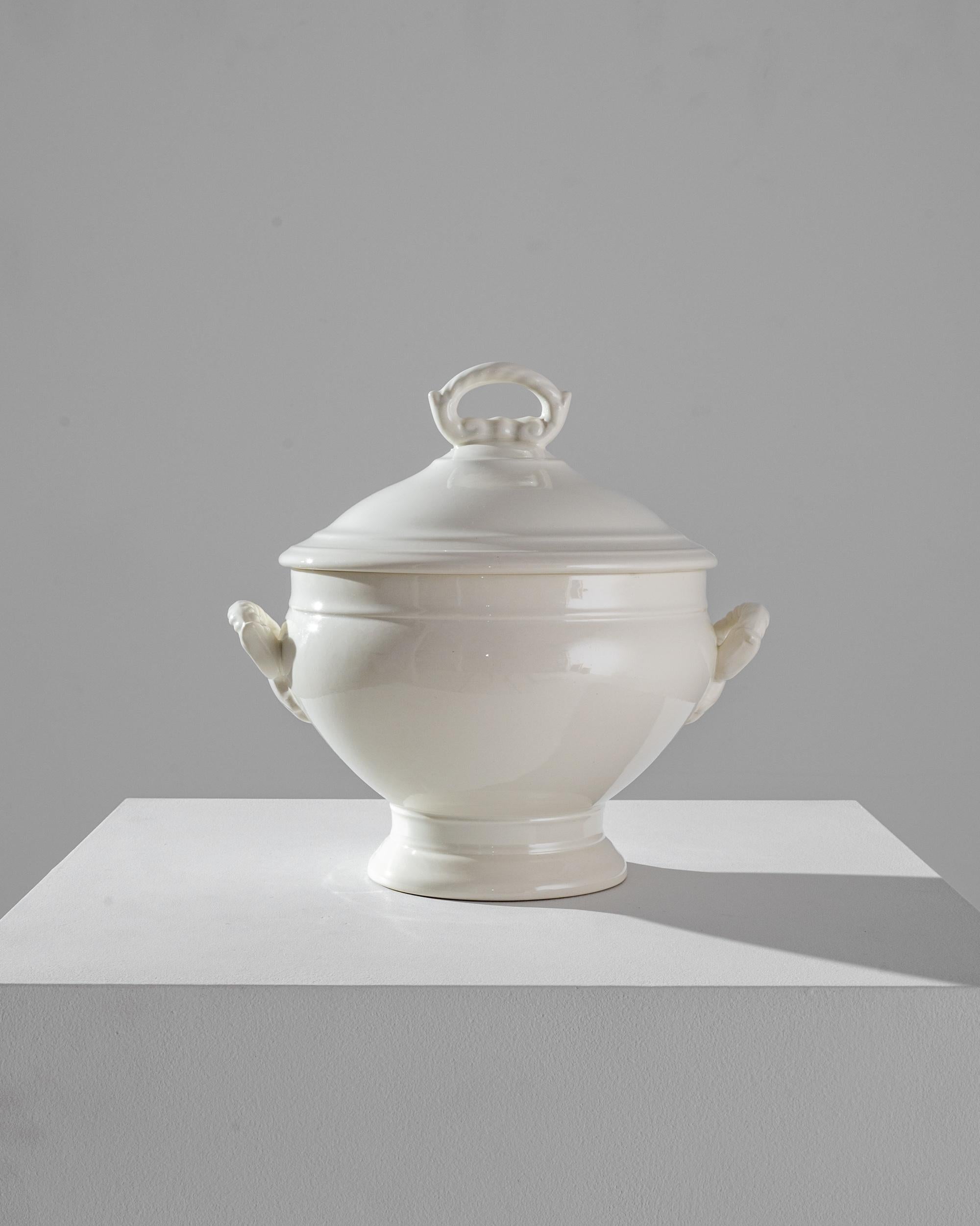 Exquisitely crafted in Belgium at the beginning of the 20th century, this porcelain vessel is especially proportioned for the delivery of liquid courses. As a serving vessel the piece is composed with the requisite pomp, outfitting will all the