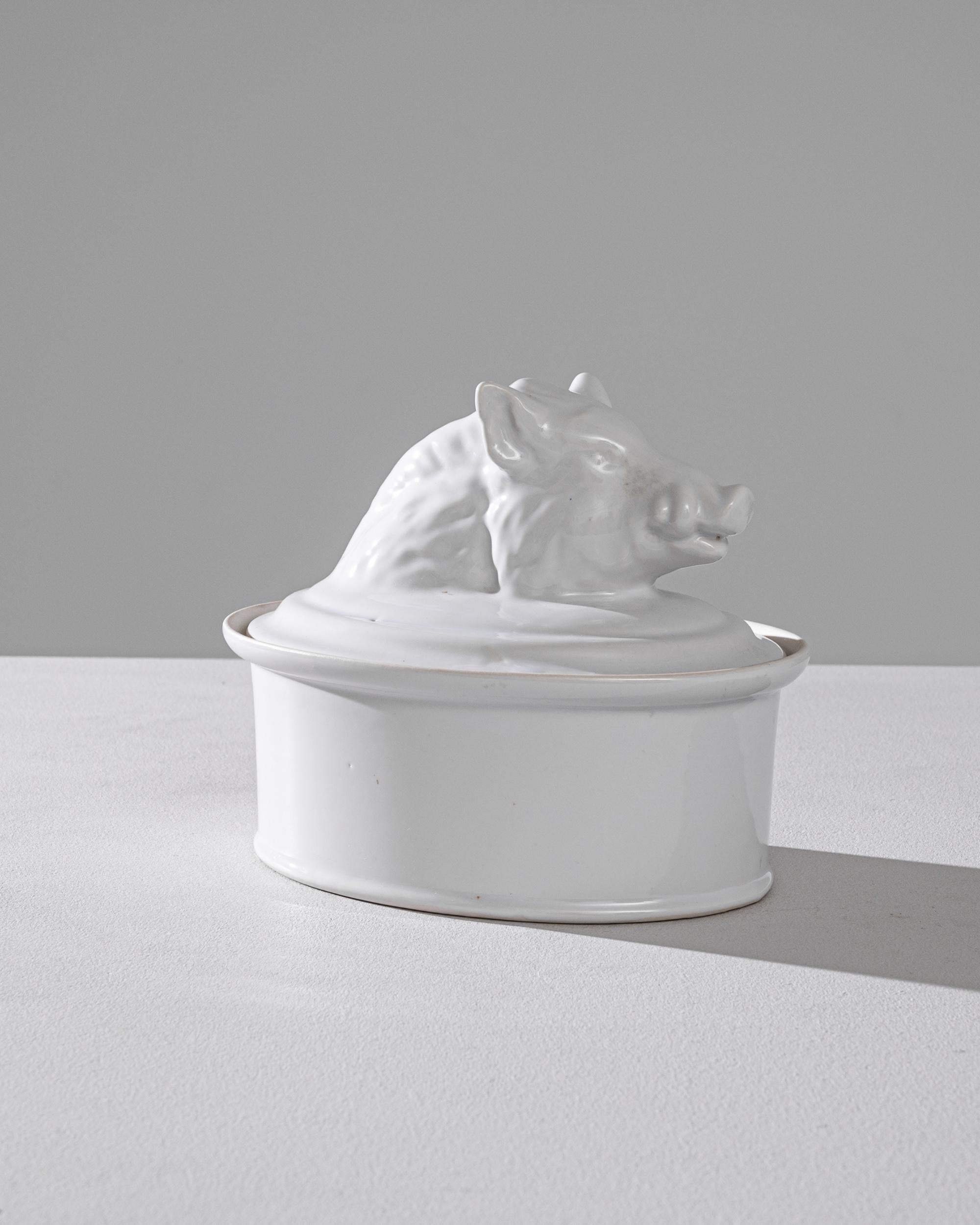 A porcelain tureen with lid from Belgium, produced circa 1900. An antique tureen with a clean unmarred surface like a new bar of soap, allowing, without distraction, the prominent wild boar bust that seems to emerge from the lid to take center stage.
