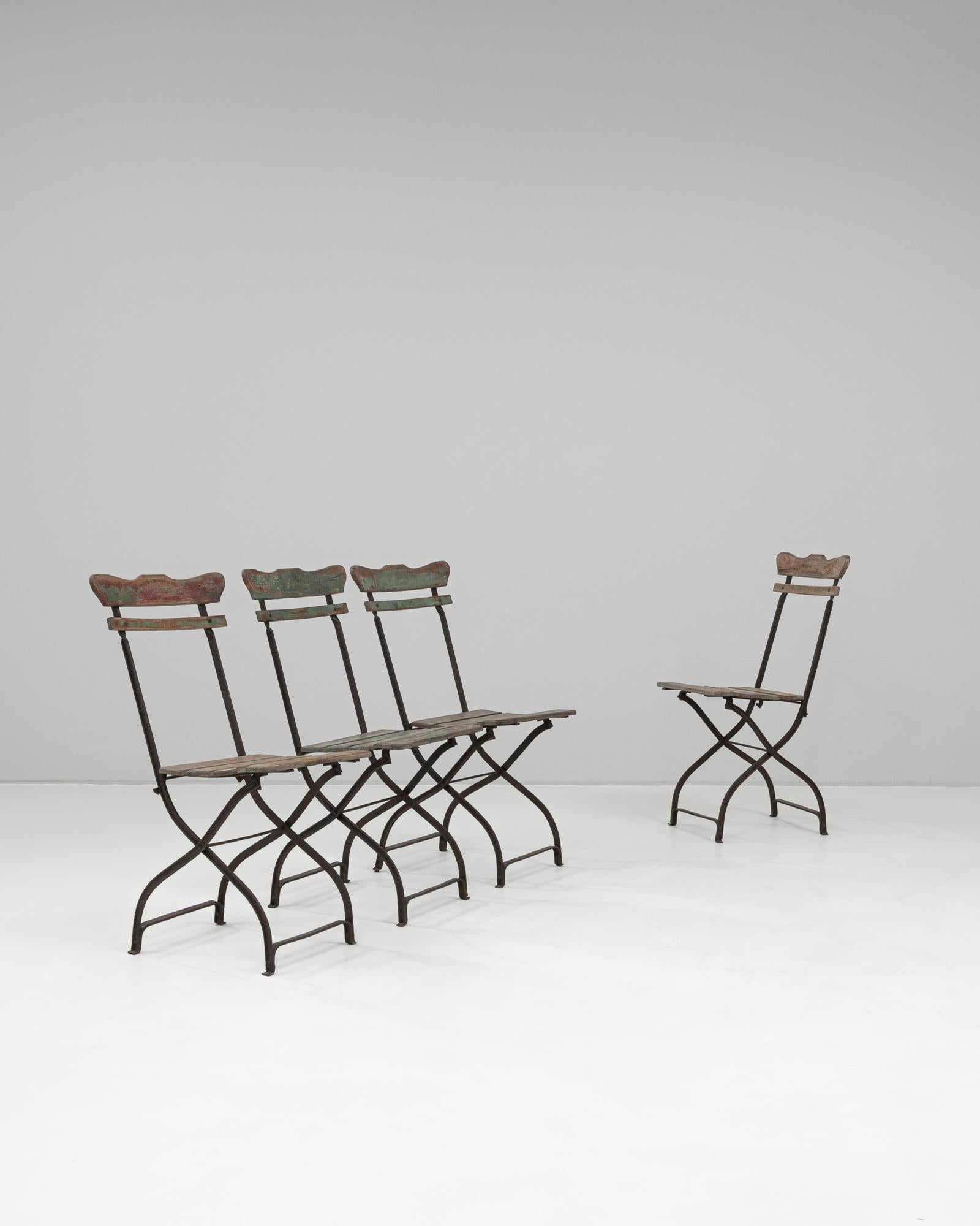This set of four garden chairs from 1900s Belgium beautifully blends rustic charm with functional design. Each chair features a gracefully curved iron frame with a folding mechanism, providing both durability and ease of storage. The wooden slat