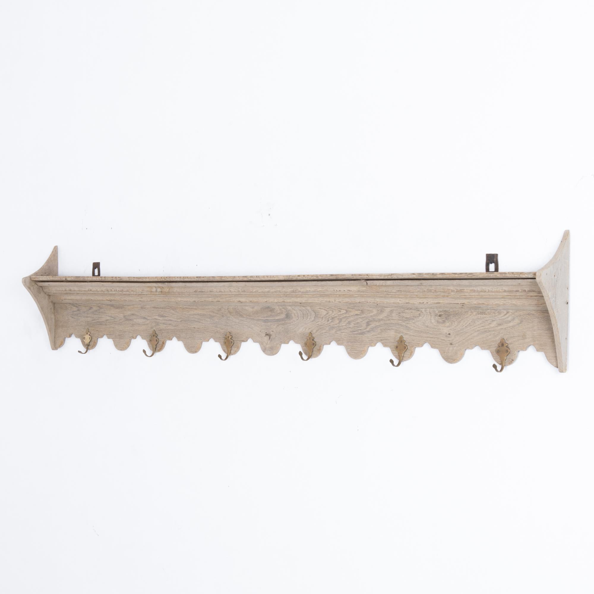This wooden wall coat rack was made in Belgium, circa 1900. It offers a charming accent on any wall, with its crown molding, scalloped panel, and curved triangular side brackets. Hang coats, hats, or accessories on six U-hooks adorned with delicate