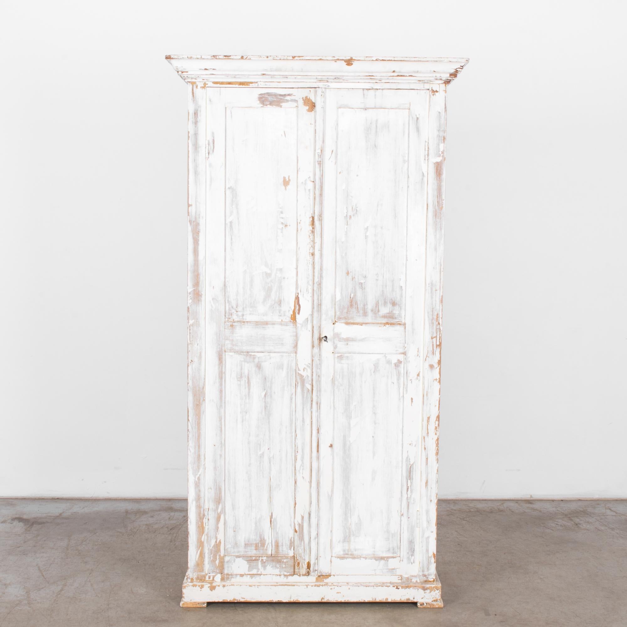 A white wood patinated armoire from Belgium, circa 1900. Handcrafted armoire standing on small feet fitted with four shelves and a pole for hanging. A refreshing space maker, stylish storage, a cosmopolitan closet. Old world grandeur for modern city