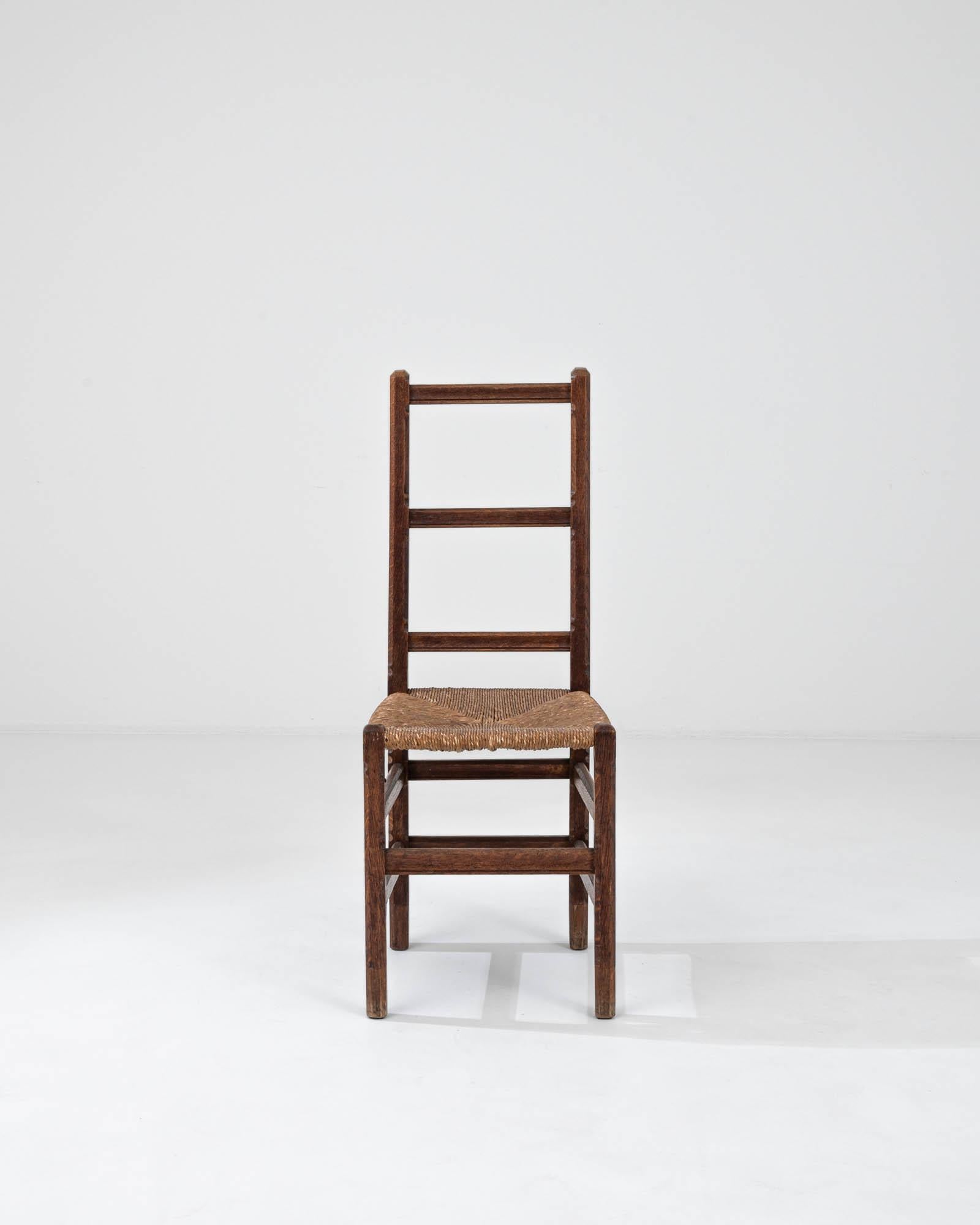 Realizzata in Belgio nei primi anni del 1900, questa sedia con schienale a scaletta in legno è un esempio di design rurale europeo tradizionale. Lo schienale alto e verticale con doghe orizzontali uniformemente distanziate crea un senso di