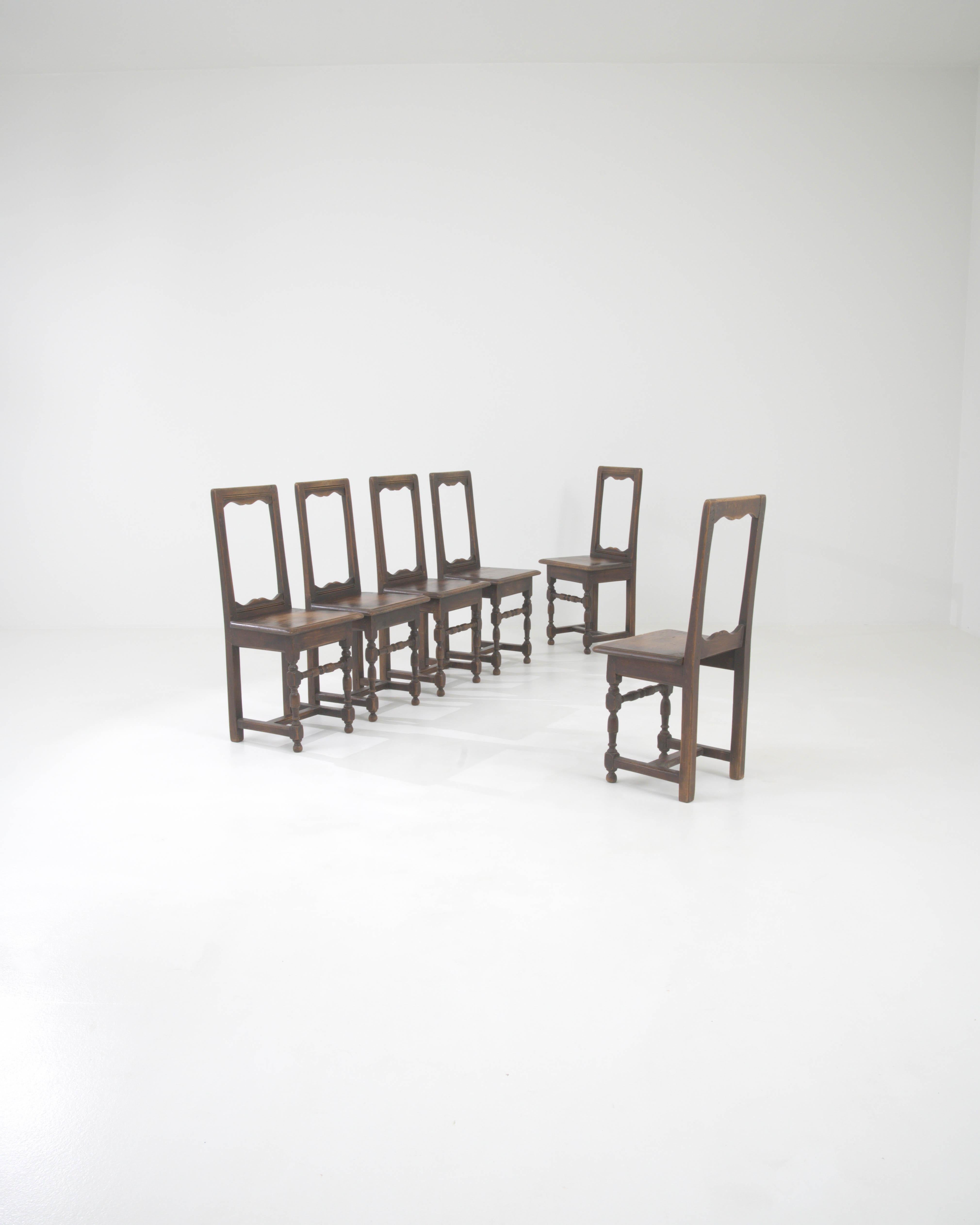 Step back in time with this magnificent set of six 1900s Belgian wooden dining chairs, a testament to the enduring elegance of early 20th-century design. Each chair boasts a strong, dark wooden frame with a rich patina that tells its own unique