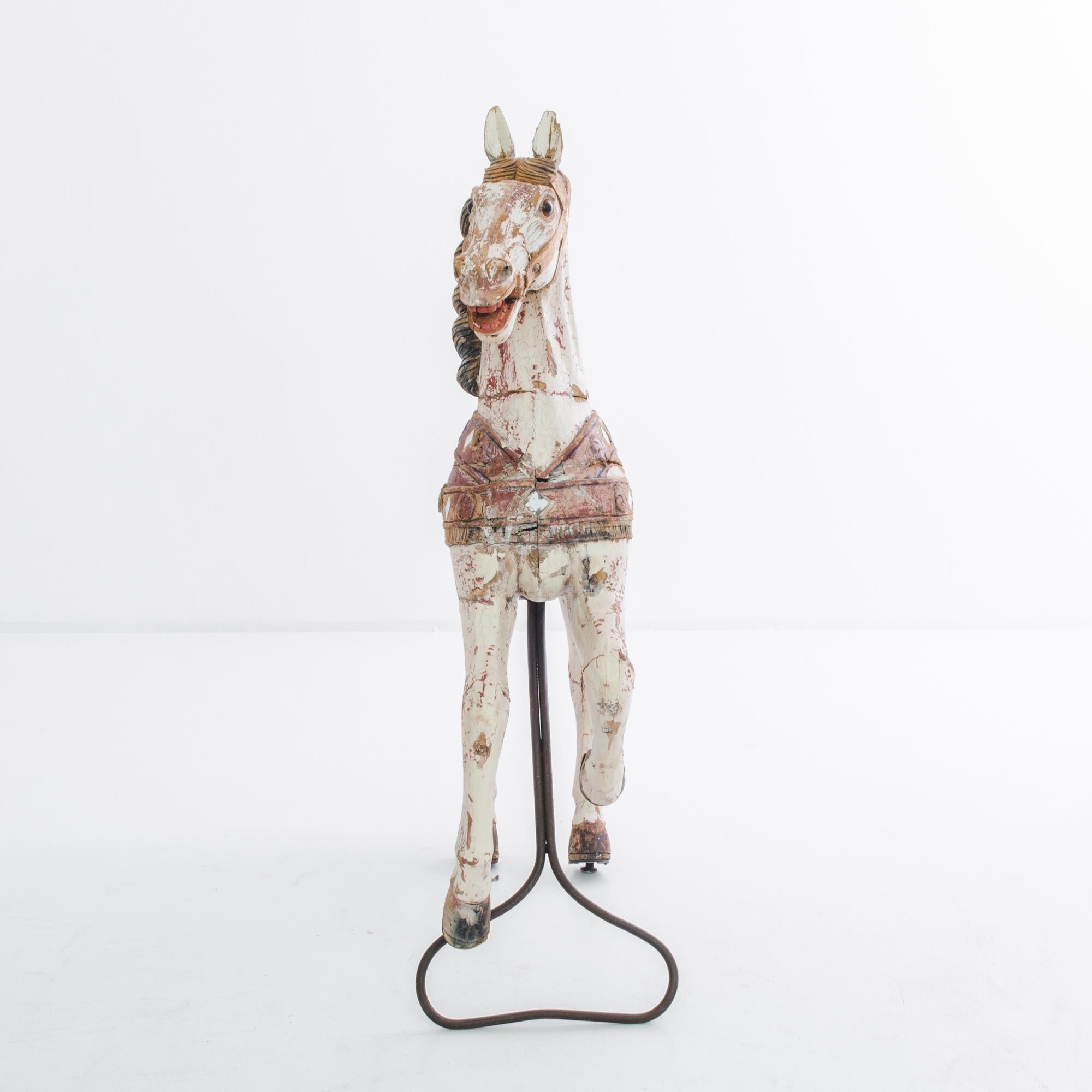 A wooden horse, made in Belgium, circa 1900. The horse is positioned in a dynamic pose, front legs raised in a canter. A flowing mane, decorative saddle and tack, carved with fine detail. A cheery white stallion, colors fading. For your inner