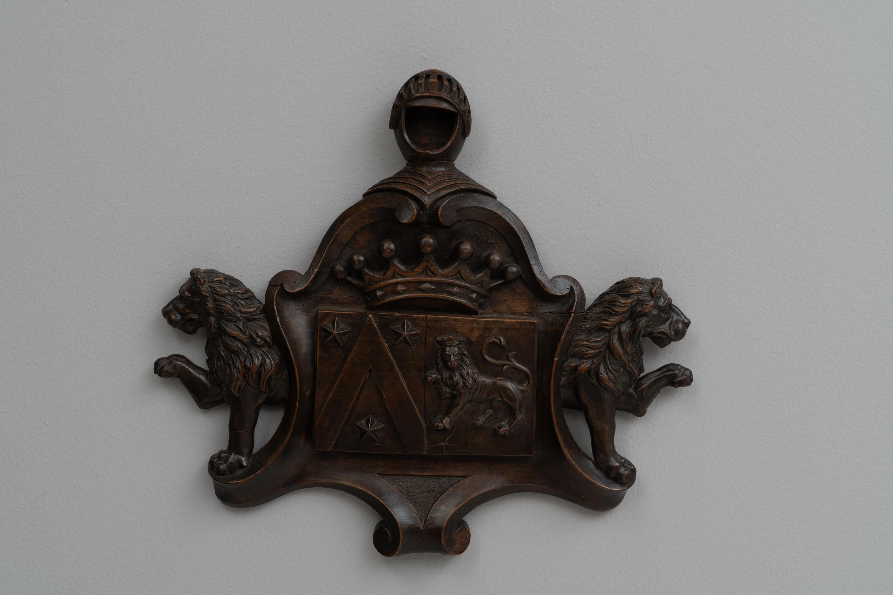 This early 1900s Belgian Wooden Wall Decoration is a magnificent piece of craftsmanship, rich with historical charm and artistic detail. Intricately carved in dark wood, it features a regal crest flanked by two robust lions, symbolizing strength and