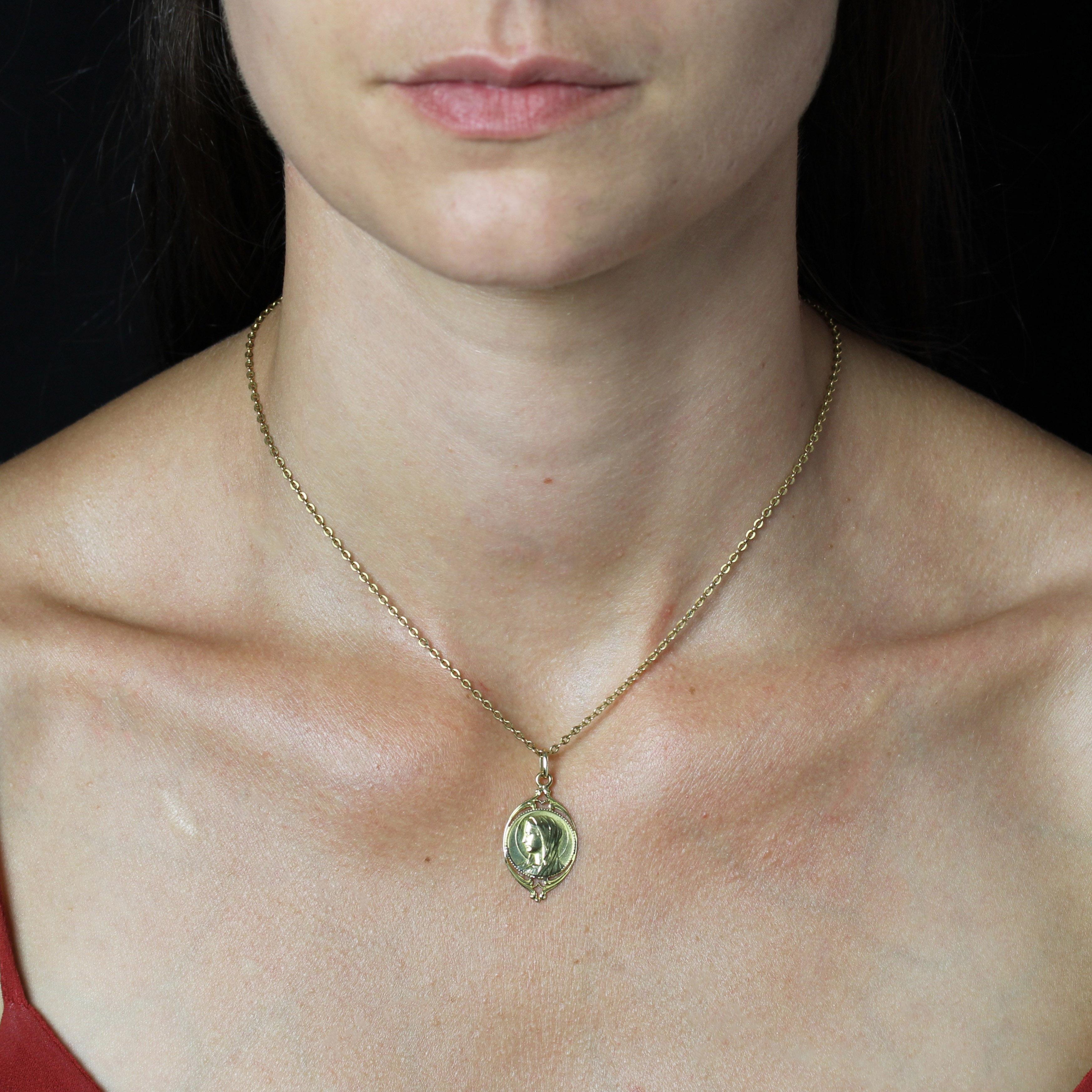 Medaille aus 18 Karat Gelbgold.
Ovale Medaille mit durchbrochener Arabeskenverzierung, die die mit einem Heiligenschein versehene Jungfrau Maria inmitten einer Perlenverzierung zeigt. Die Rückseite ist mit den Initialen graviert.
Der Anhänger wird