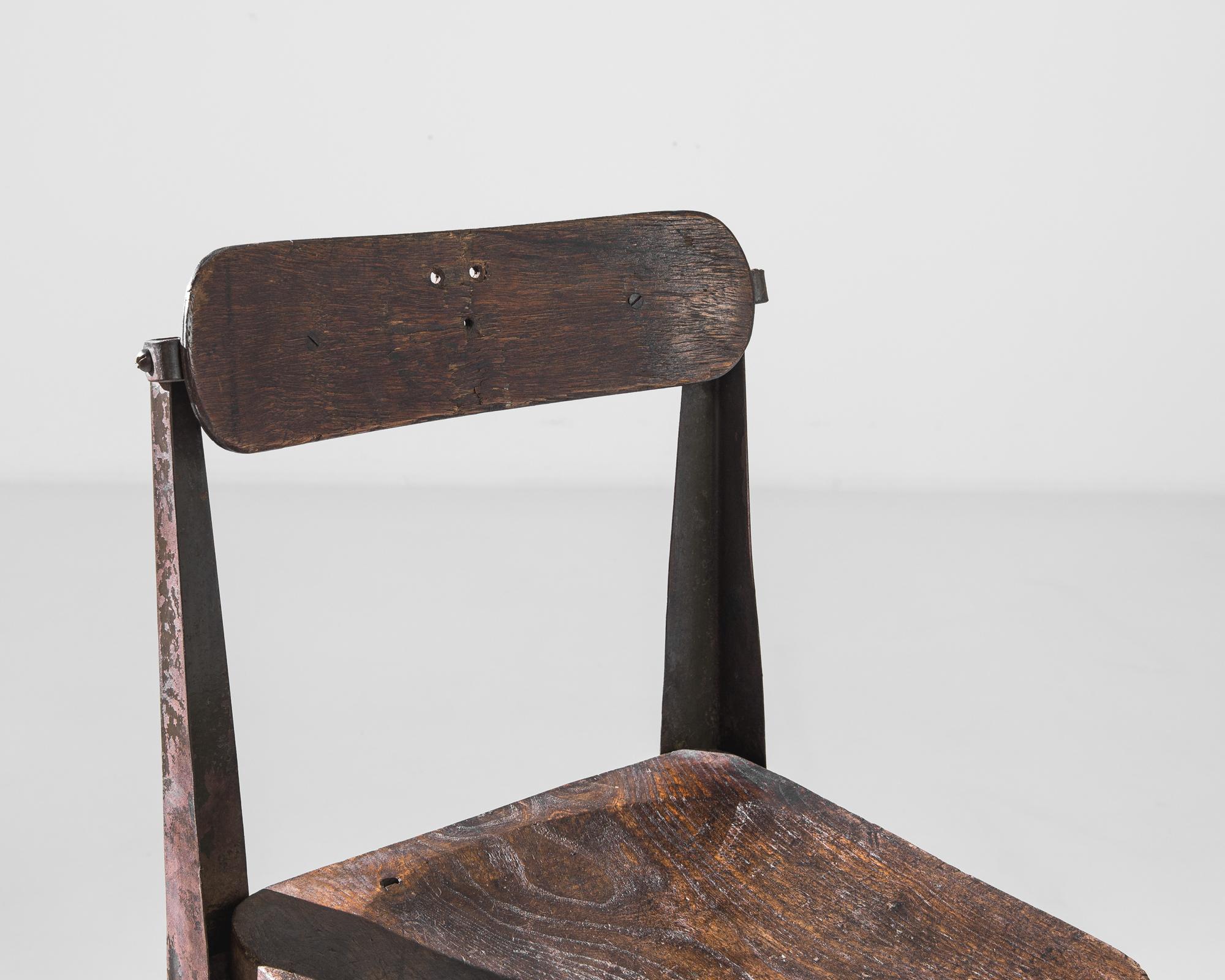 A metal chair with wooden seat and back from the United Kingdom, produced circa 1900. A metal frame accent chair with four L-shaped, slightly angled legs connected by an x-shaped stretcher, featuring an adjustable hinged wooden seat back. This seat