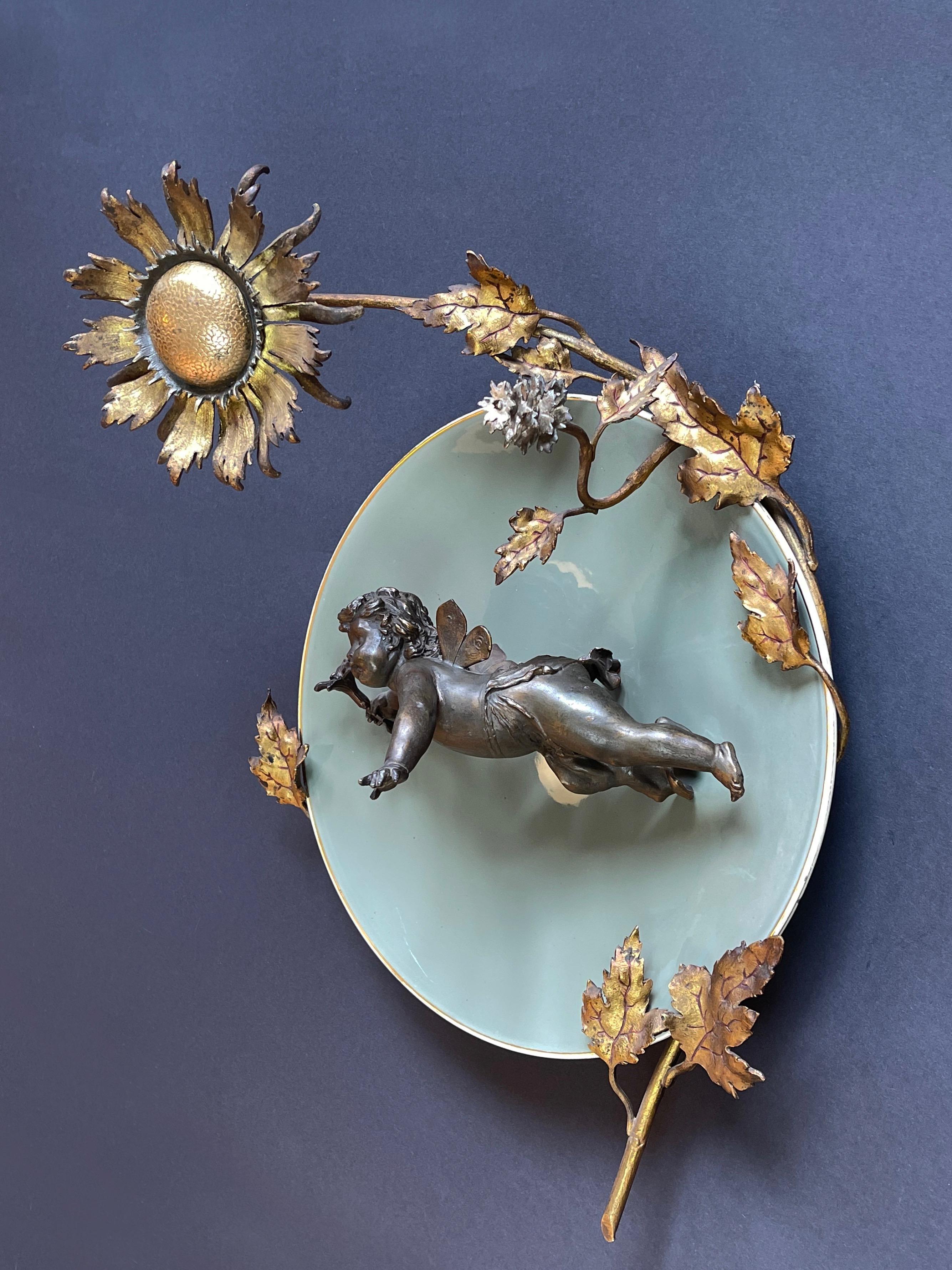 Wonderfully presented bronze cupid with gentian flower, held by golden rimmed, light olive green ceramic plate.
Framed by beautifully hand crafted and decorated gilt metal tendrils and leaves  of a truly impressive sunflower, like a glowing