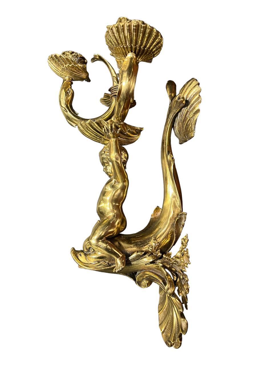 A circa 1900’s Caldwell gilt bronze single sconce with cherub on a dolphin holding 3 lights on shells and one light on top shell. Large size and impressive details.