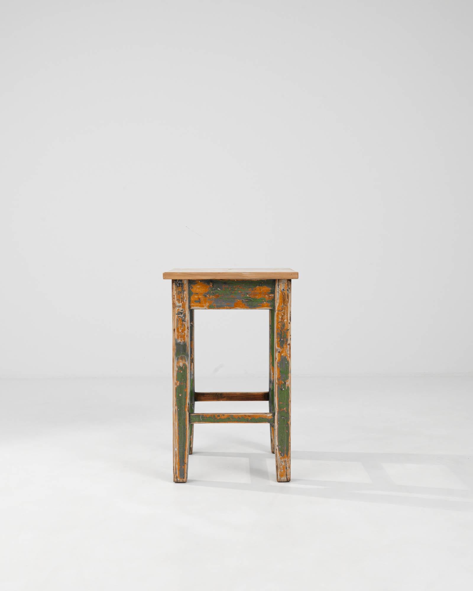 This 1900s Central European Wood Patinated Side Table is a testament to the enduring charm of vintage furniture. Its frame, awash with layers of peeling green and orange paint, reveals a storied past, adding a rich, textural depth that new