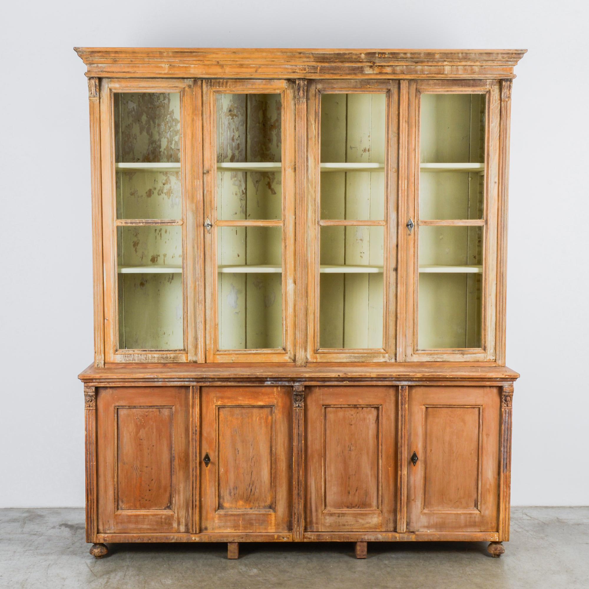 A softwood vitrine from Central Europe, circa 1900 with a beautiful age patina. This tall and timeless vitrine features two upper cabinets with glass-paneled double doors and two lower cabinets with wood-paneled double doors, separated by a shallow