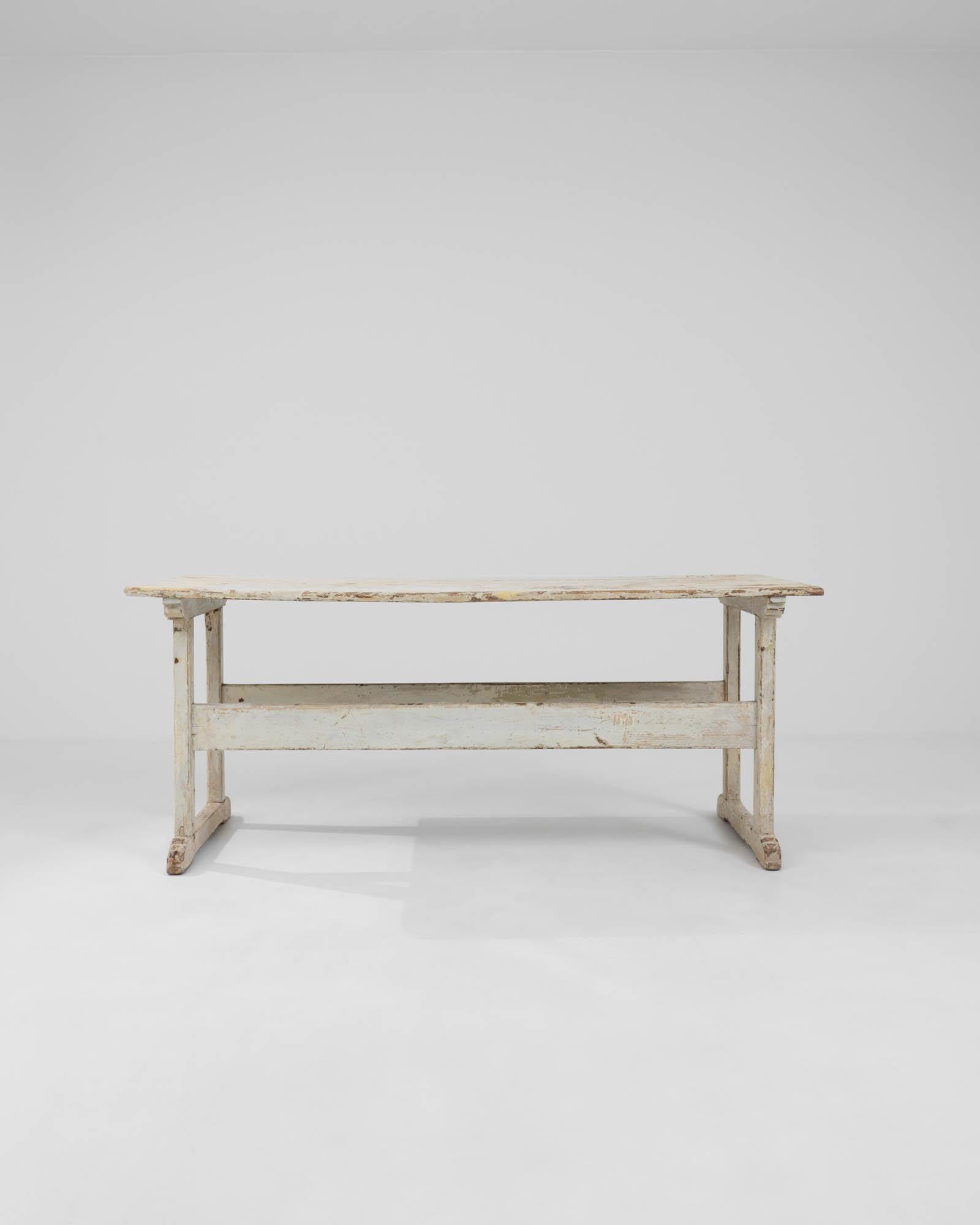 Imbued with a sense of rustic nostalgia, this early 1900s Central European wood table is a splendid artifact of simpler times. The white patinated finish, weathered through decades, reveals a story in every scratch and layer, inviting a touch of