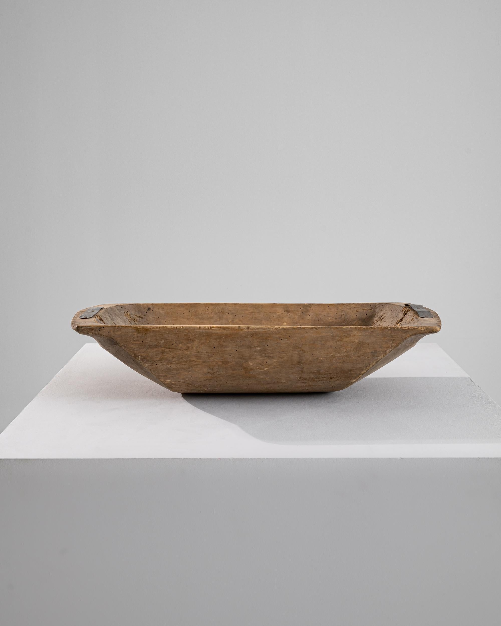 A wooden bowl made in 1900s central Europe. A simple yet curious artifact, this bowl was created from hollowing out one solid piece of wood. Once used to hold rising dough, weathered metal bands and networks of aged and gnarled wood remind of its