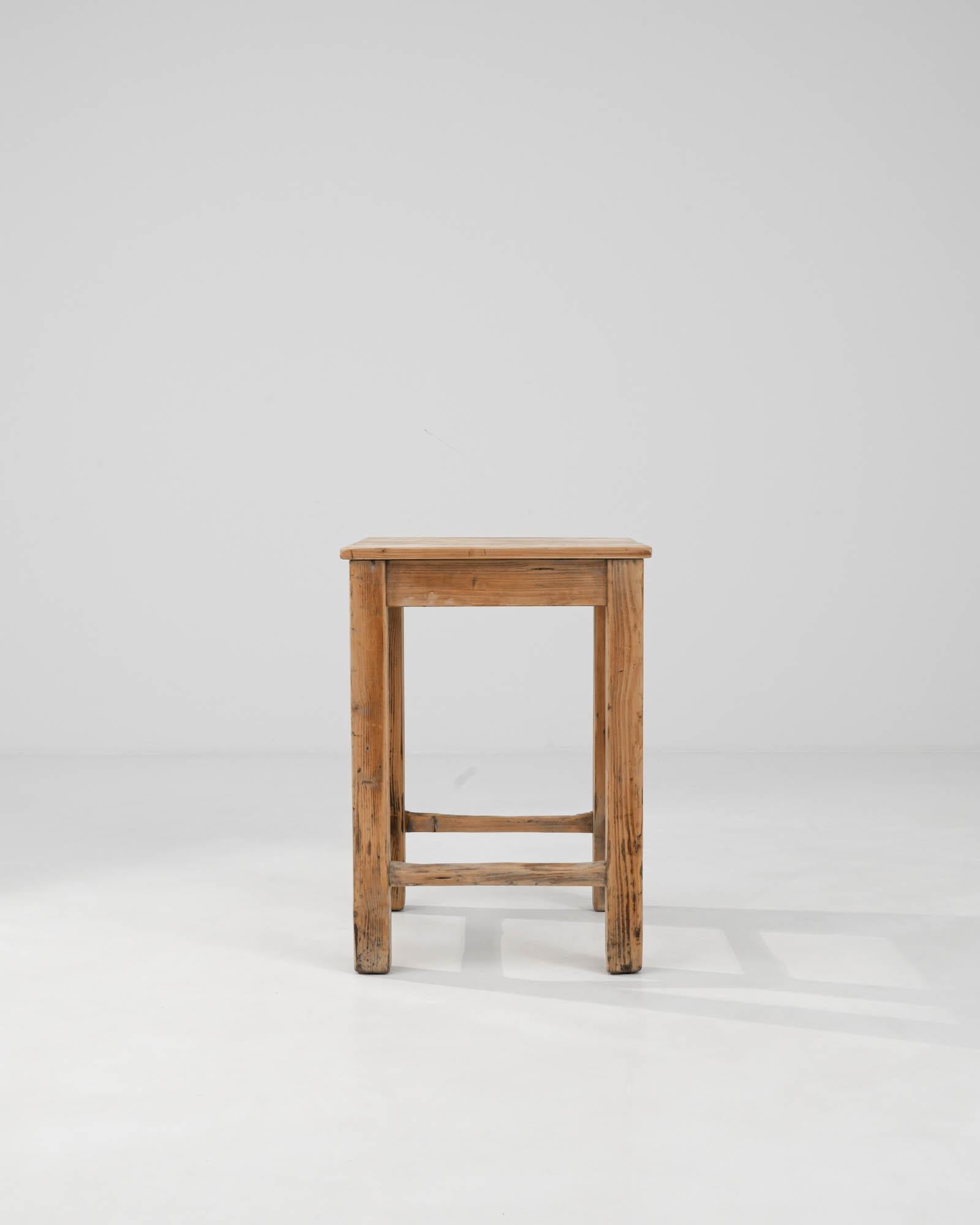 This 1900s Central European Wooden Side Table embodies the unassuming elegance of early 20th-century craftsmanship. Constructed from sturdy, well-aged wood, it boasts a natural finish that highlights the grain and character of the timber. The