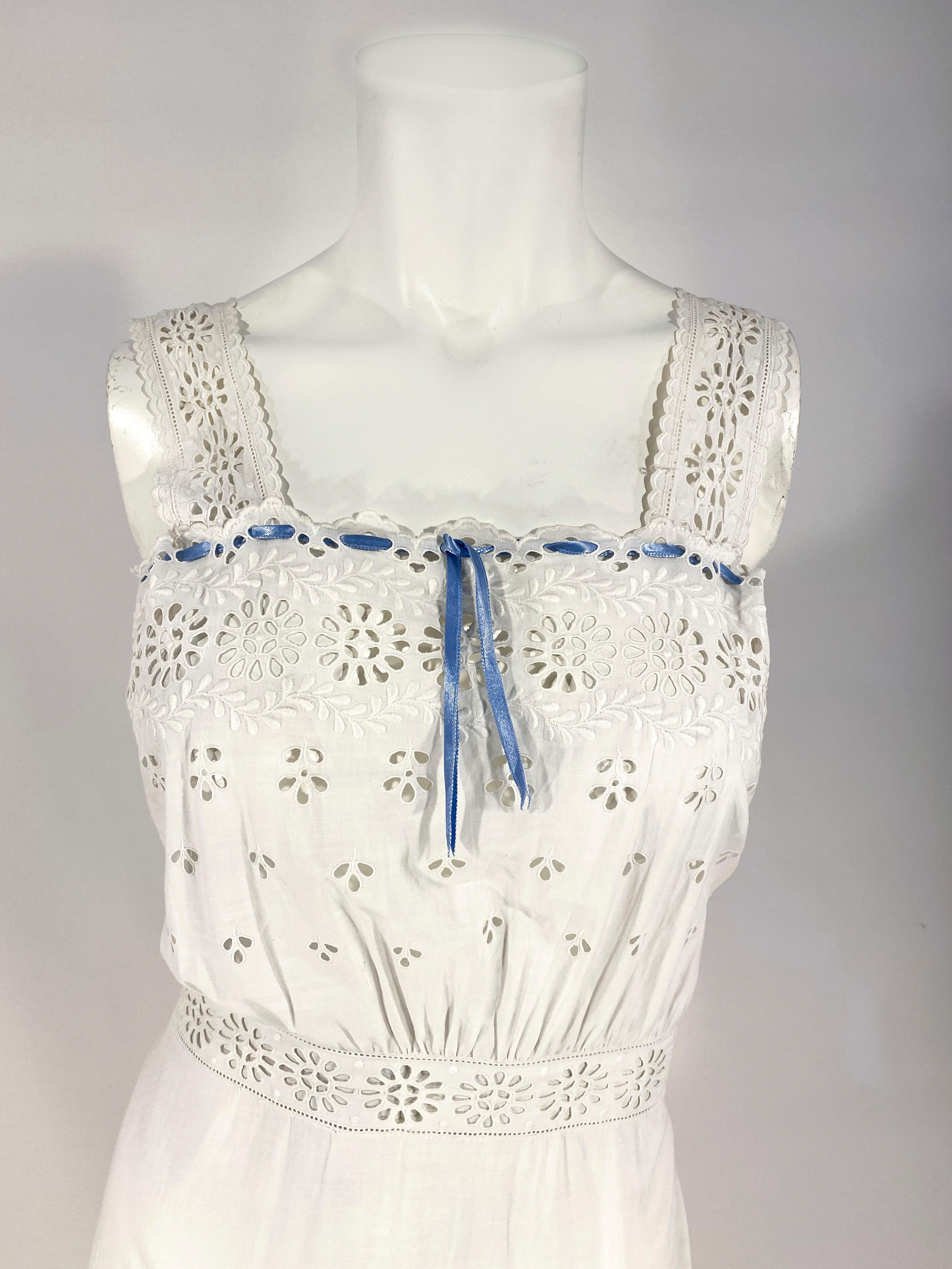 1900s Edwardian whit cotton under petticoat that could easily be worn as a day dress. The garment features eyelet patters, machine embroidery, bands of eyelet trim on skirt and straps, and a ruffled hem. The top of the bust has a blue silk ribbon to