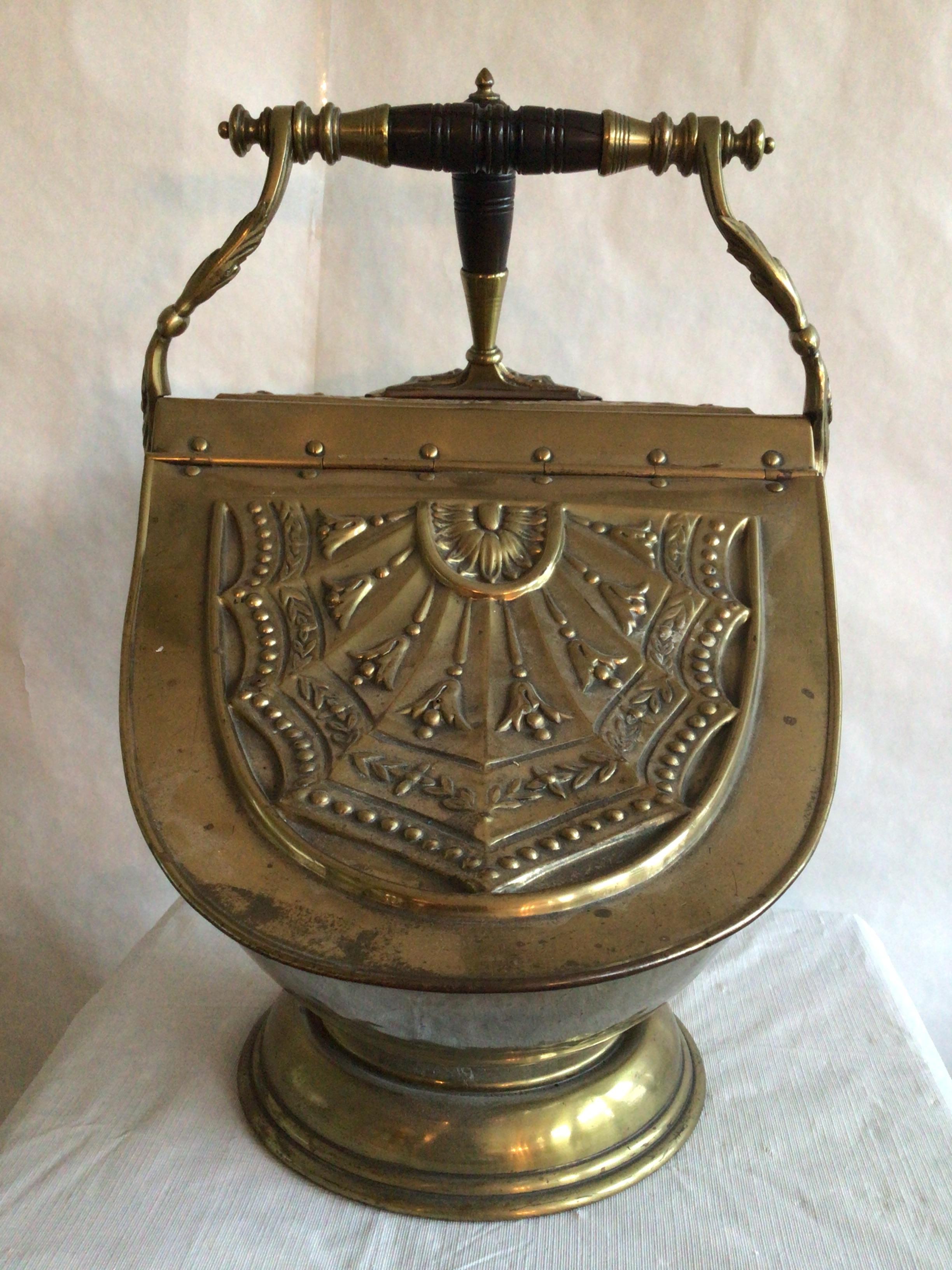 Navetta per carbone inglese del 1900 in ottone con pala 
Accentuato da dettagli in rilievo
Coperchio con cerniera
Manico in legno tornito

Alcune piccole ammaccature - crepa nel manico di legno