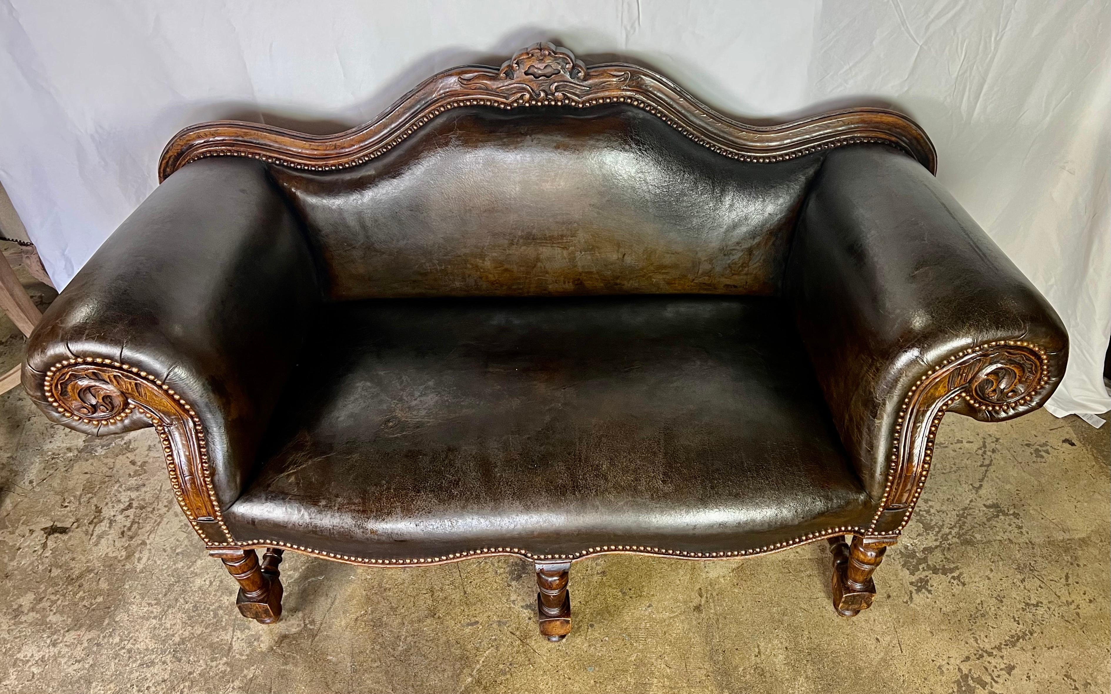 Early 20th Century Georgian leather rolled arm settee.   The back has an eyebrow shape with carving at the top.  The sofa stands on six legs that are connected by a bottom stretcher. Leather is distressed by is still intact.