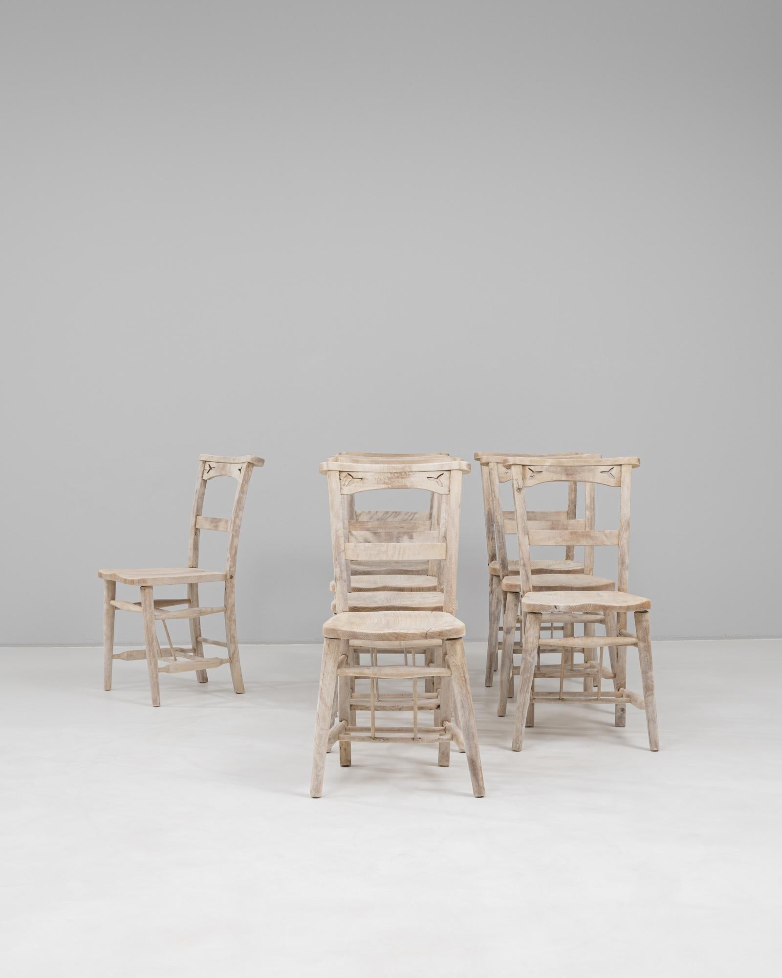 This 1900s English set of eight oak dining chairs presents a charming blend of rustic simplicity and subtle decorative detail. Each chair features a gently curved backrest with a carved motif near the top rail, lending a handcrafted, almost