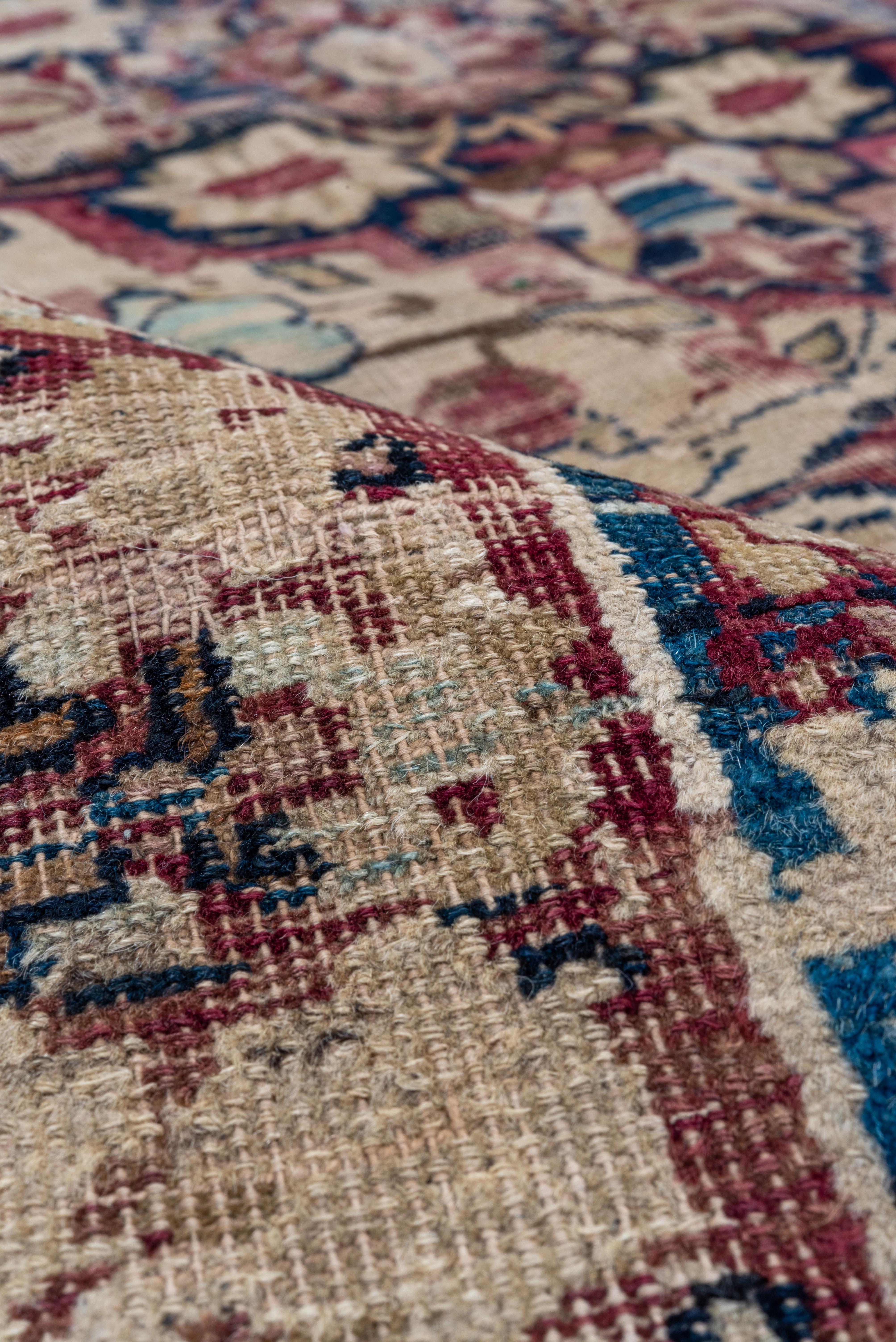 This Persian city carpet shows a central navy clawed and pendanted medallion, with lateral en suite half medallions and smaller stepped floral lozenges, all on a cream ground with closely conforming flower trails. Cream border with quadruple simple