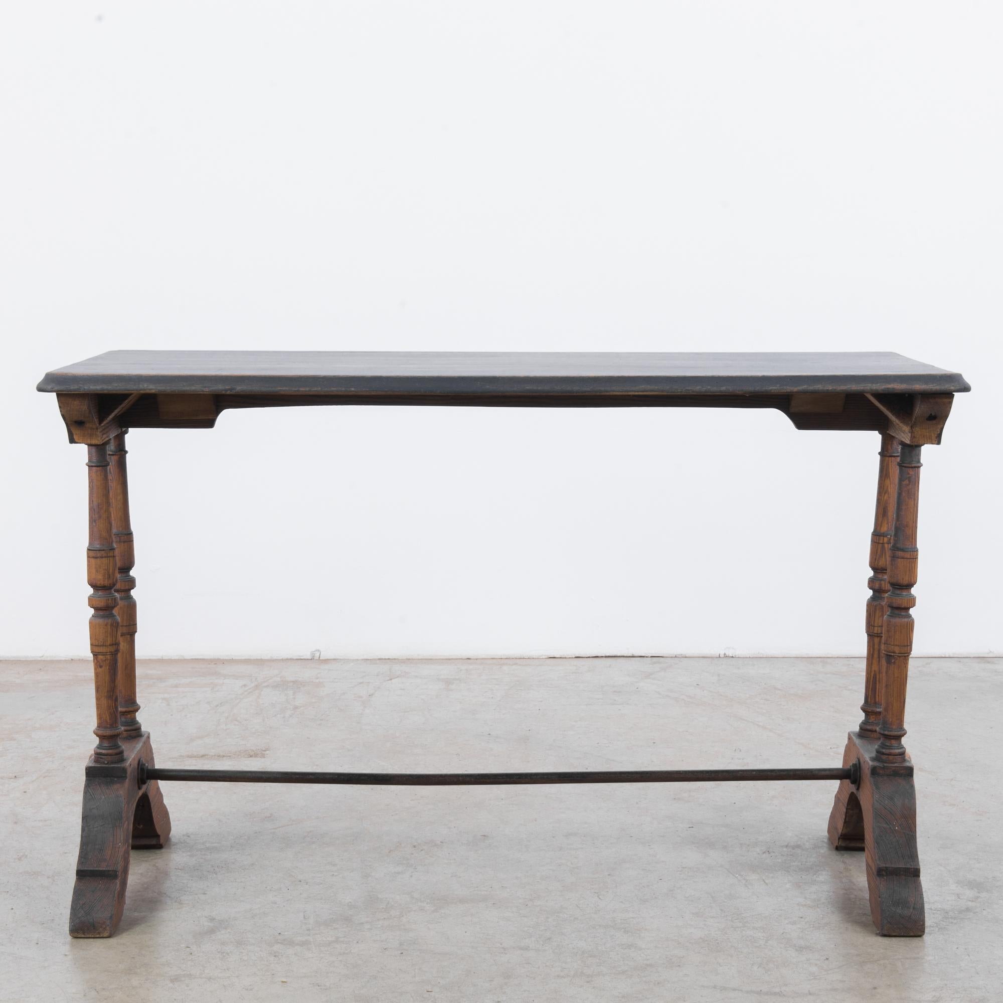 A wooden bistro table from France, circa 1900. A tall, narrow rectangular silhouette; slender turned legs sit atop contoured brackets, joined by a metal strut. The black-painted surface of the tabletop has weathered into a stylish patina, while the