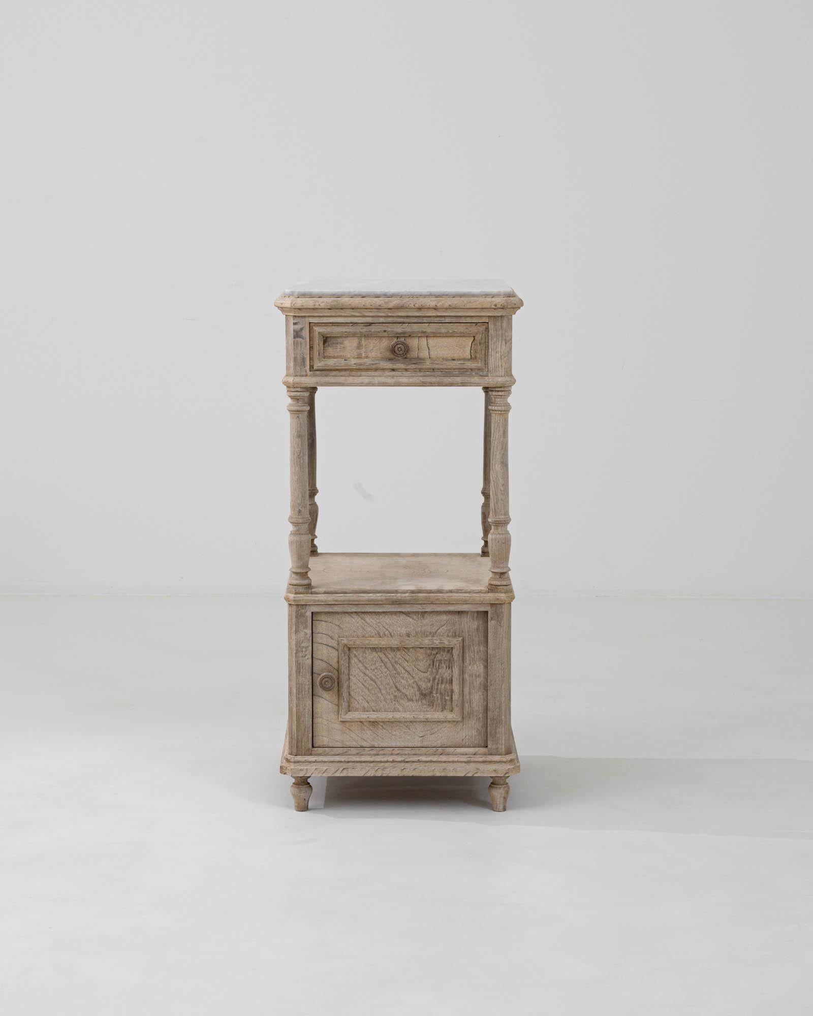 Embrace the quaint charm and refined simplicity of the early 1900s with this exquisite French Bleached Oak Bedside Table, crowned with a timeless marble top. The subtle, sun-kissed hue of the bleached oak exudes a serene, lived-in elegance,