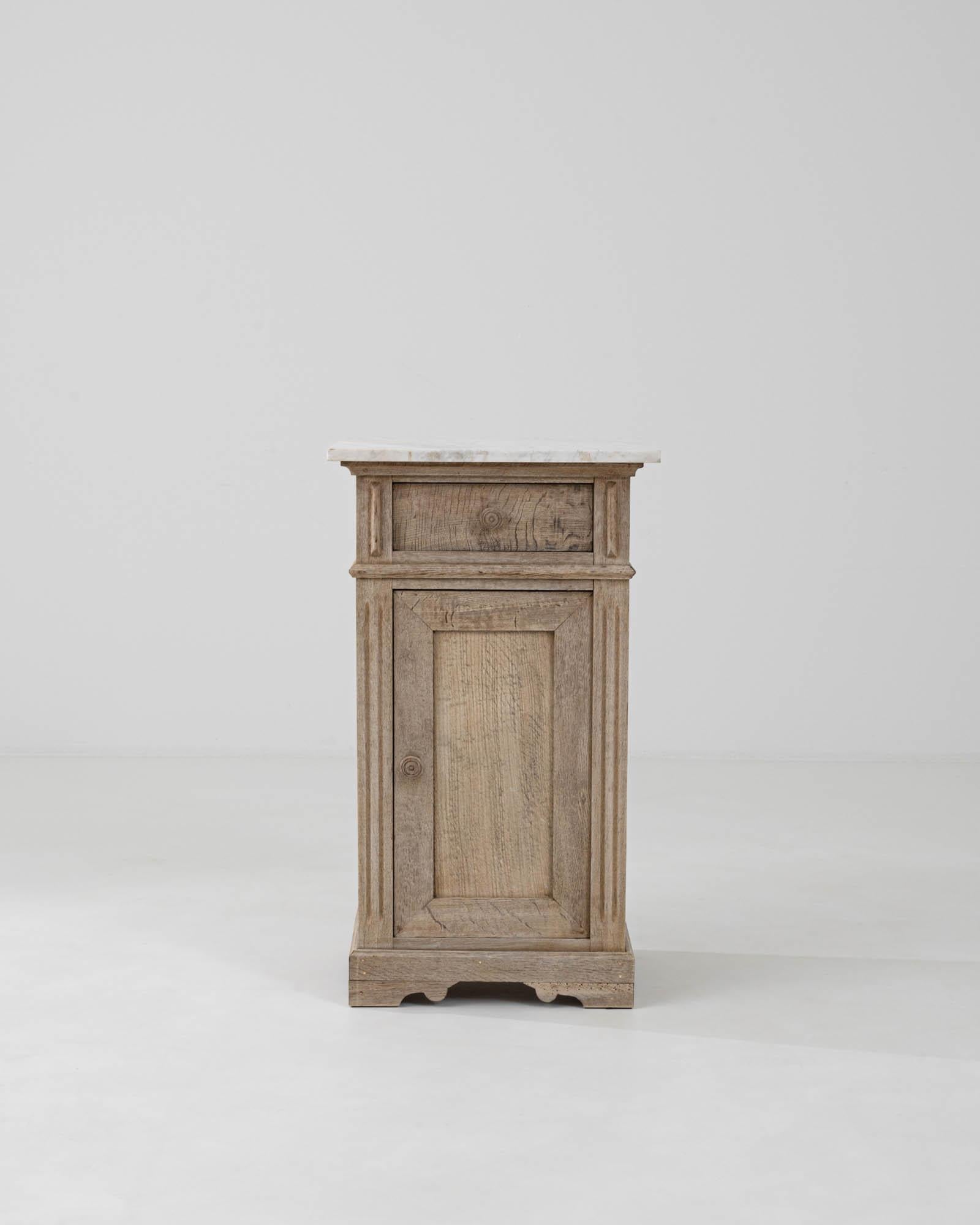 Step into the allure of provincial French design with our 1900s French Bleached Oak Bedside Table, topped with a luxurious slab of marble. The rustic elegance of the weathered oak provides a delightful contrast to the cool, polished marble, uniting