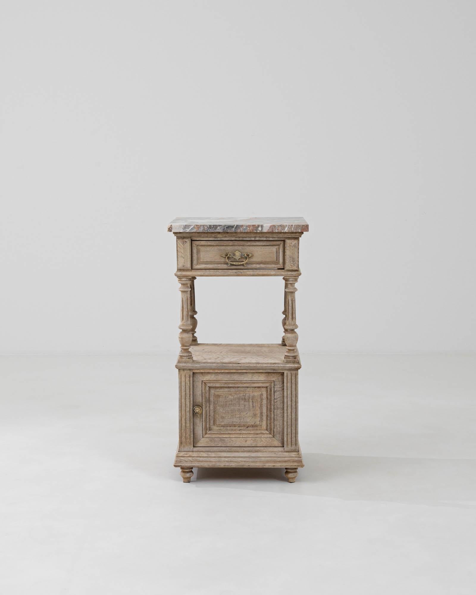 Experience a touch of timeless elegance with this 1900s French Bleached Oak Bedside Table, crowned with an exquisite marble top that exudes a sense of opulent sophistication. Crafted with meticulous attention to detail, this piece reflects the