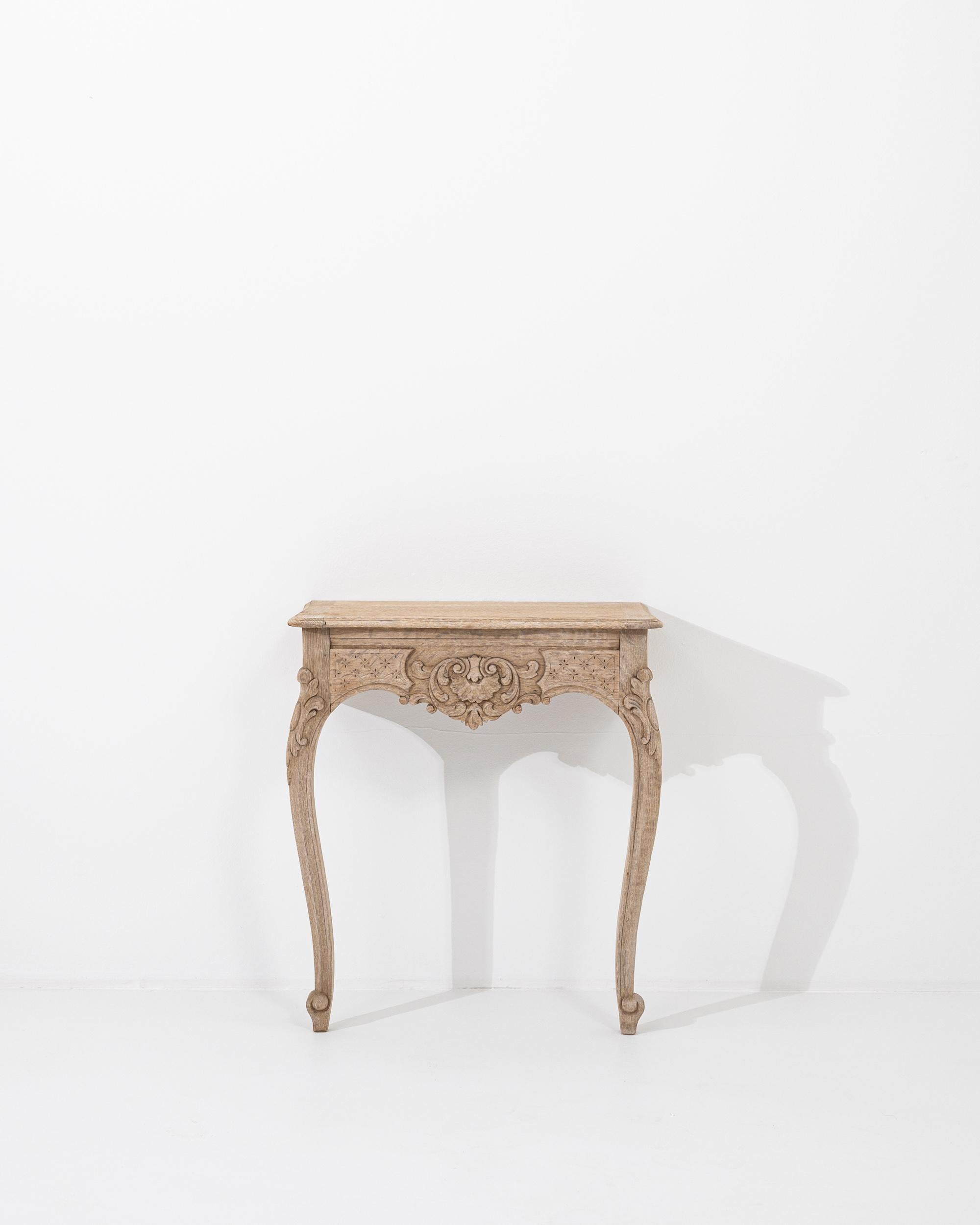A wooden console table created in 1900s France. This elegant console table appears to simply emerge right out through the wall to extend its sumptuously curved legs. Lavishly embellished floral and geometric motifs are hand-carved across its