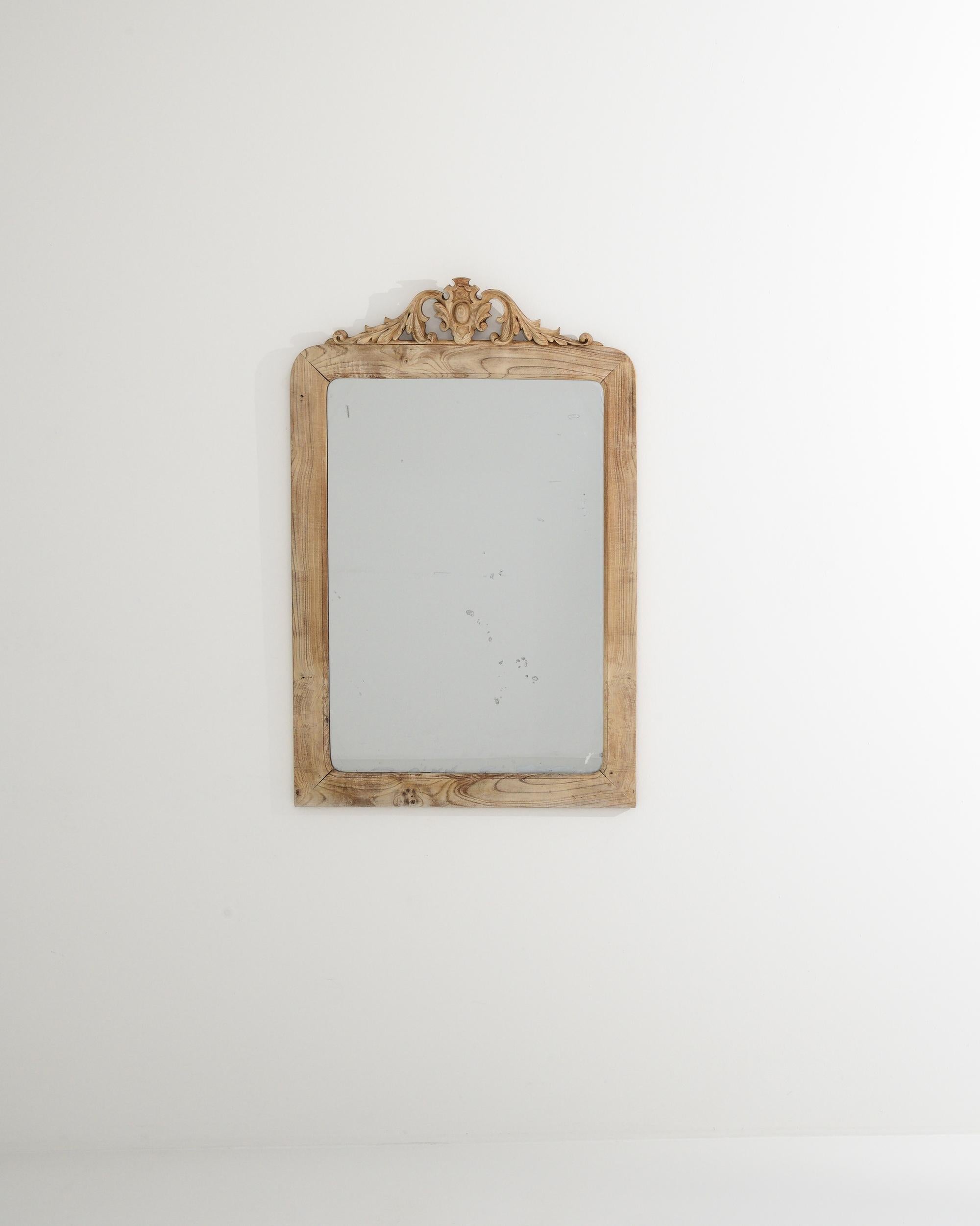 The raw, bleached oak frame enveloping this early 20th-century looking glass imparts an elegant simplicity, complemented by the natural patterns of the wood. The mirror's top is embellished with meticulously carved Acanthus leaves, evoking the