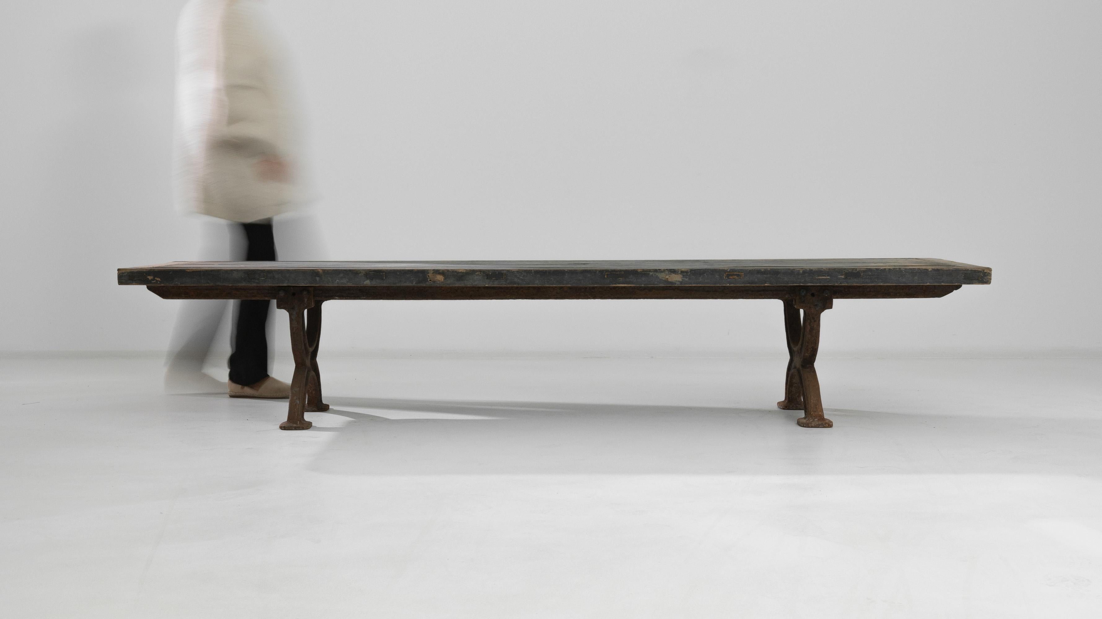 A cast iron coffee table with wooden top from France, produced circa 1900. Long and low-slung, this table with a cast iron frame sits heavy like an affixed bench. Featuring a pair of softly curved X supports connected by rust coloured stretchers,