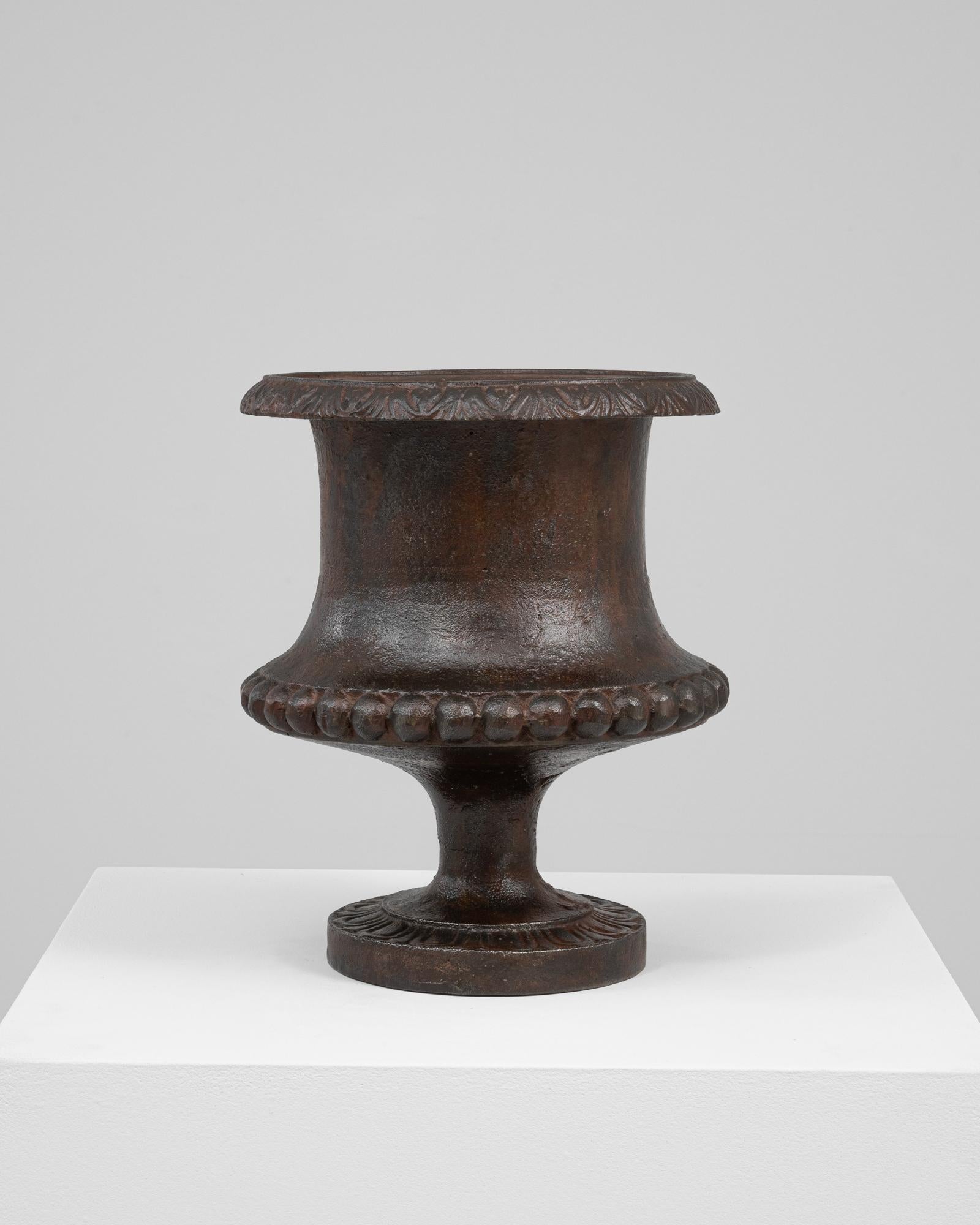 This 1900s French cast iron planter features a graceful silhouette with finely executed decorative details that reflect classical influence and period craftsmanship. The wide, flared rim is adorned with a stylized leaf motif, while the body
