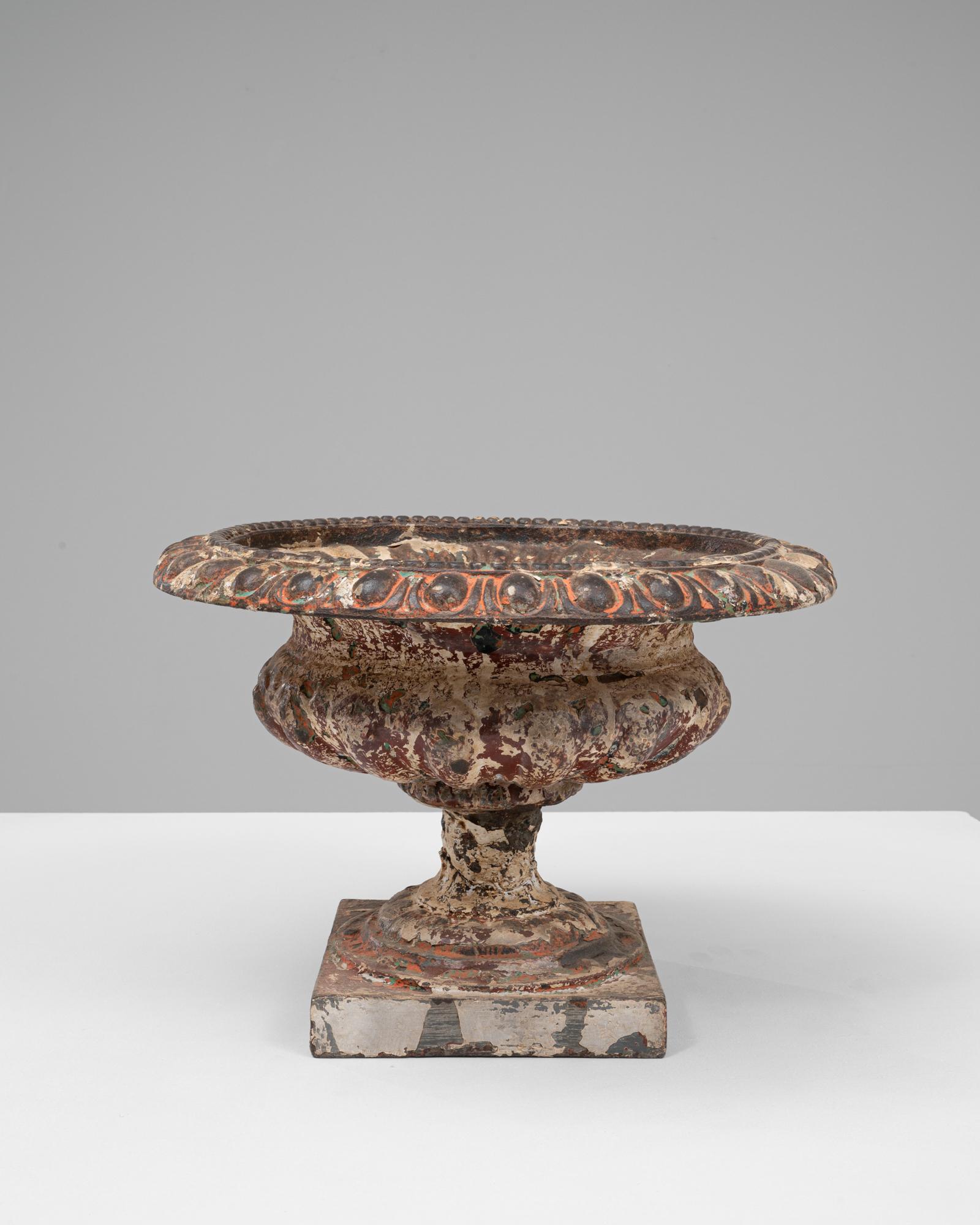 Questa fioriera in ghisa francese del 1900 presenta una patina splendidamente invecchiata che mette in risalto la sua classica forma a urna. L'ampio bordo svasato è decorato con un motivo ispirato alle uova e alle stelle, che aggiunge ritmo e