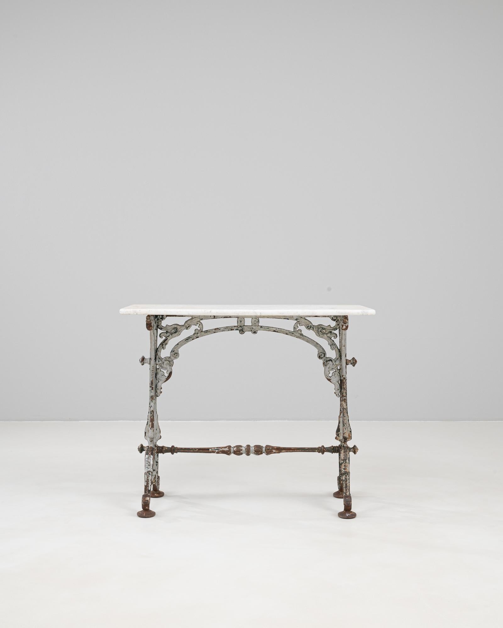 Table d'appoint en fonte française des années 1900, avec une base ornée de détails en volutes et une riche patine reflétant des années de vieillissement naturel. Le plateau en marbre blanc offre un contraste raffiné avec le cadre en métal vieilli,