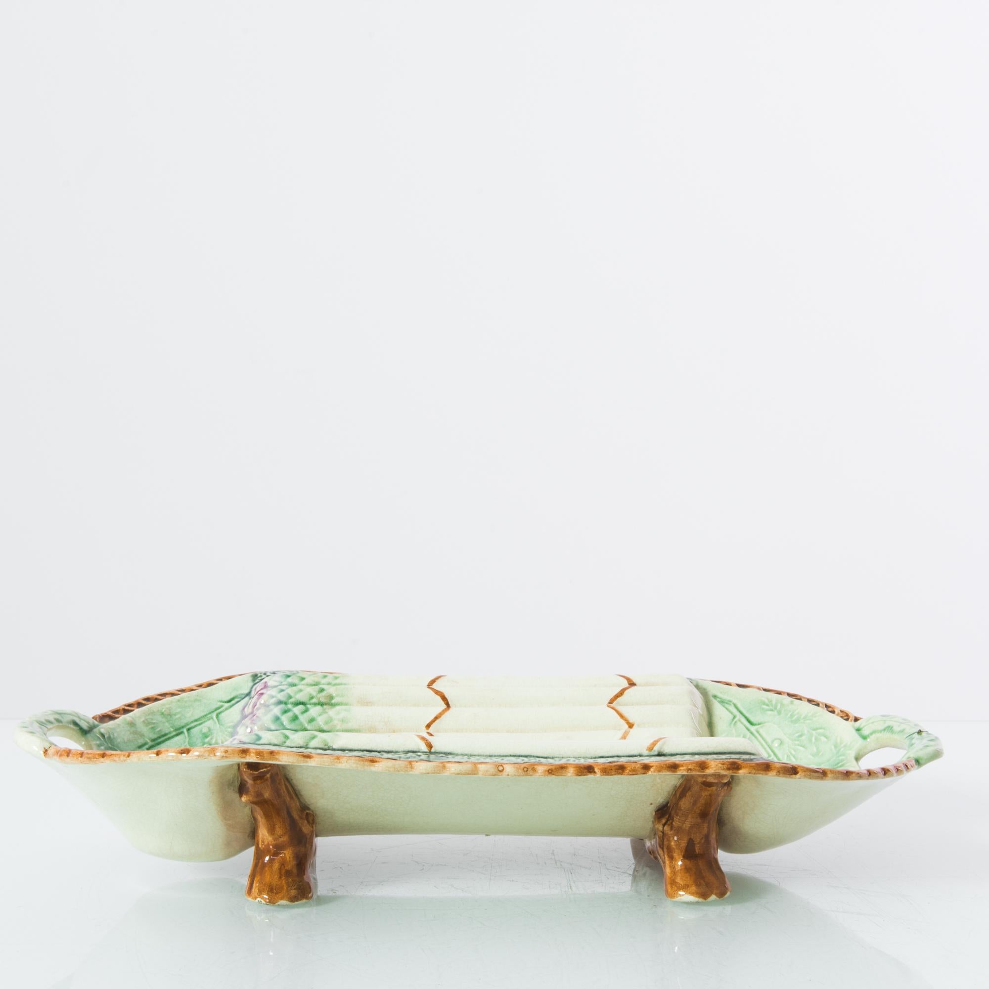 A ceramic bowl from France, produced circa 1900. An richly decorated antique bowl, featuring distinctive asparagus motifs in a delicate glaze, reflecting its intended use, propped up on two feet. Appearing with a domestic nostalgia, this enduring