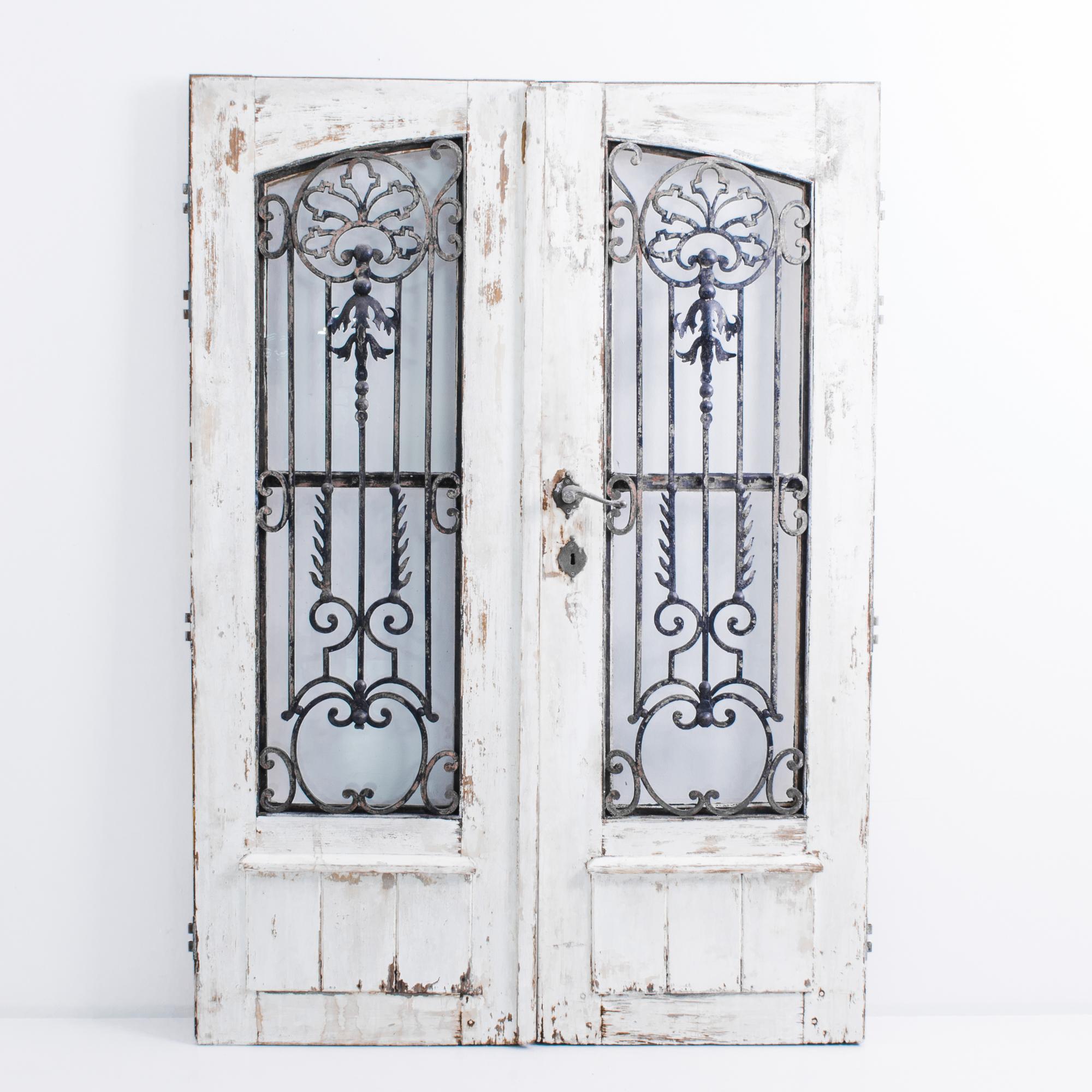 A pair of wooden doors with grille, produced in France circa 1900. Elegant wrought iron work is evocative while tastefully simplified, vertical members srpout like a seed growning into a tree. Original white patination adds a rustic ambiance to this